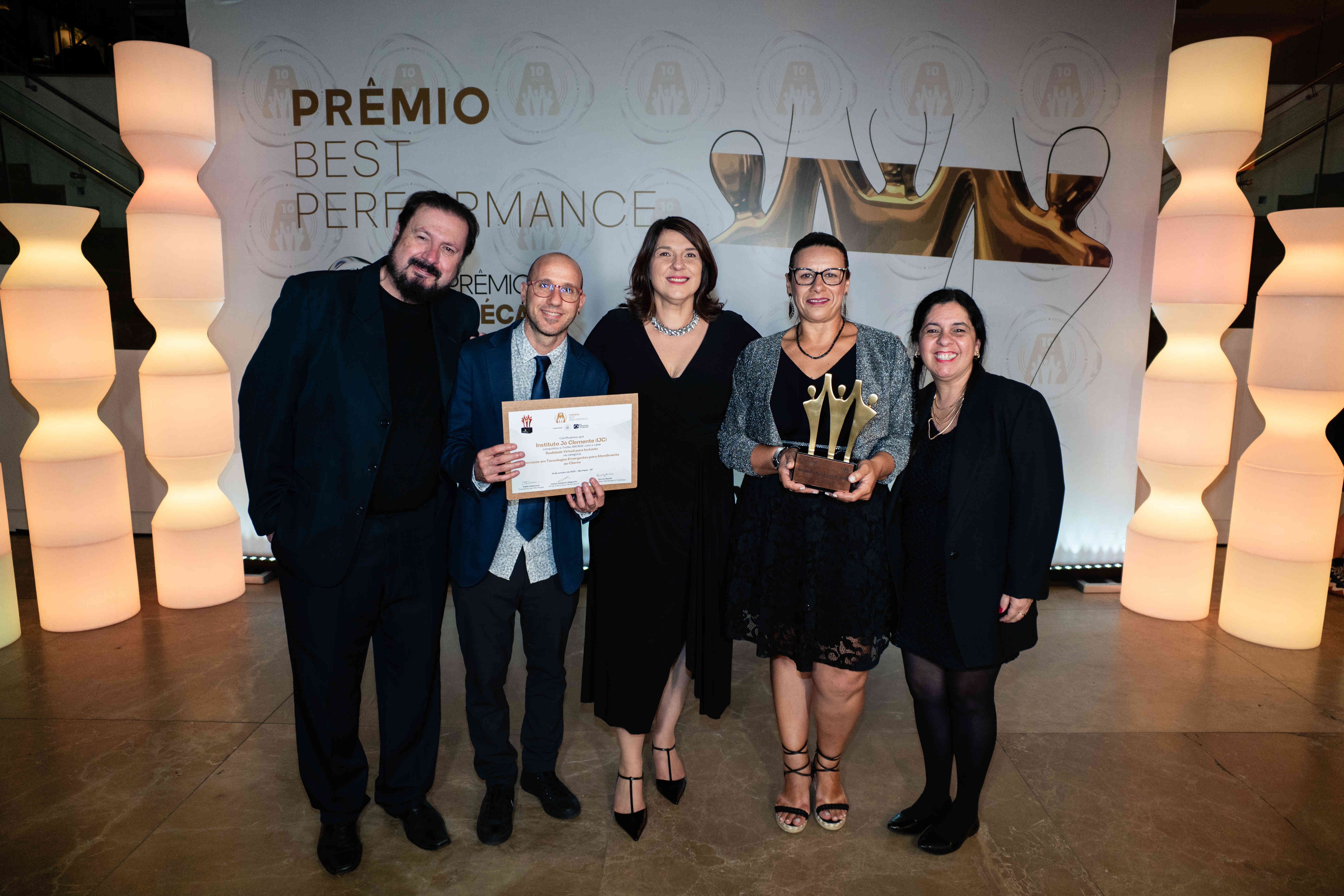 Executivos do Instituto Jô Clemente (IJC) posando com troféu bronze e certificado no palco do Prêmio Best Performance 2025