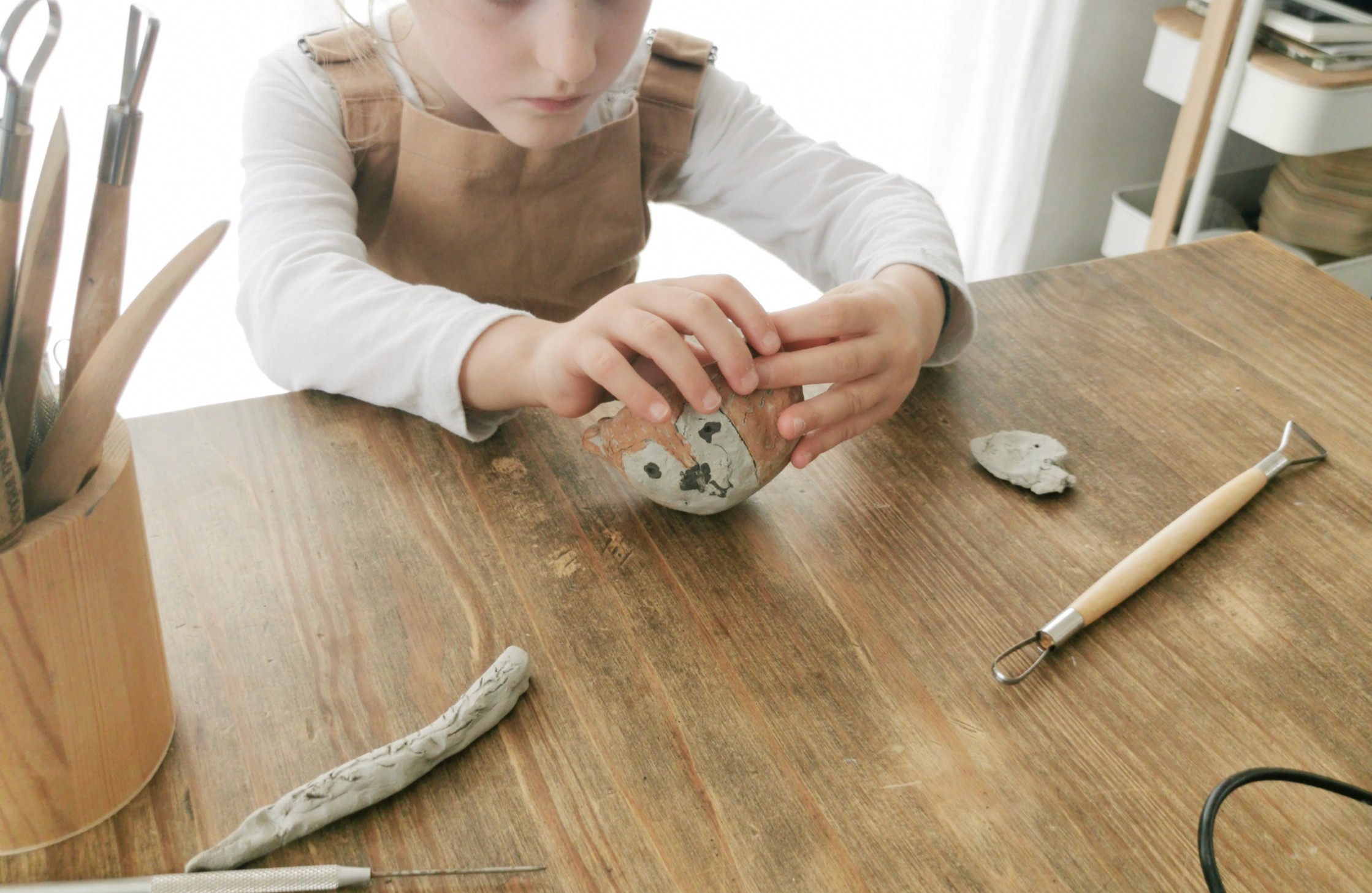 Cours céramique amulette : mains tenant une petite pièce en argile gravée de symboles, atelier Guérande