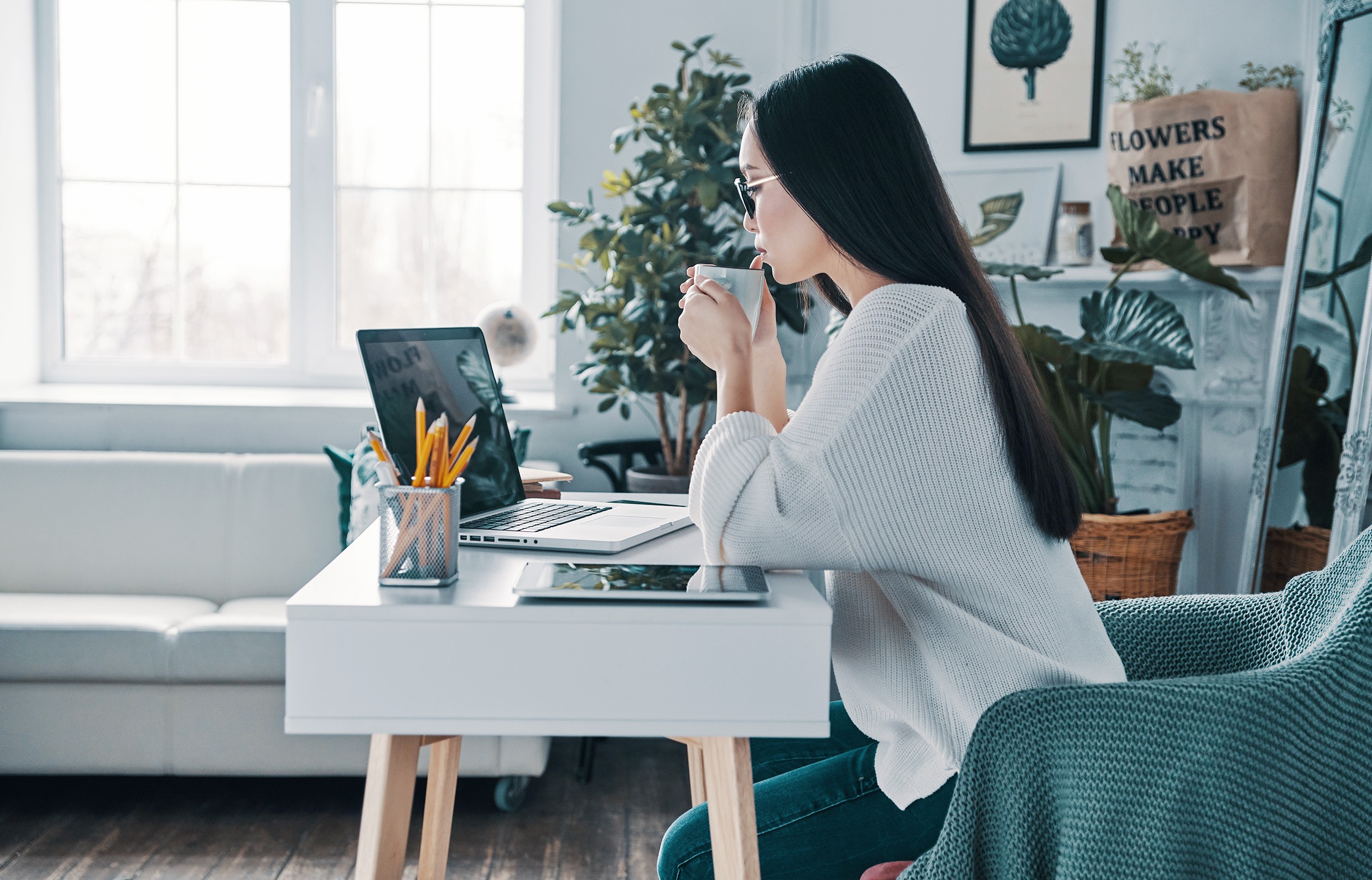 Woman working on a laptop at a desk while drinking coffee