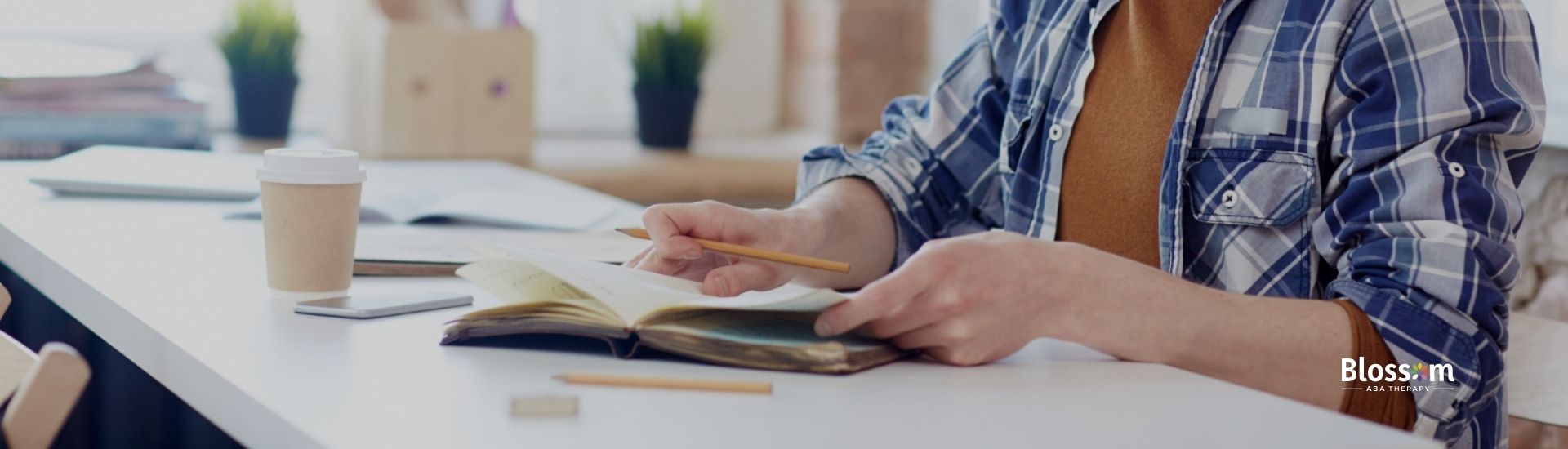 Young man in a plaid shirt studying at a desk with books studying for the BCBA exam.