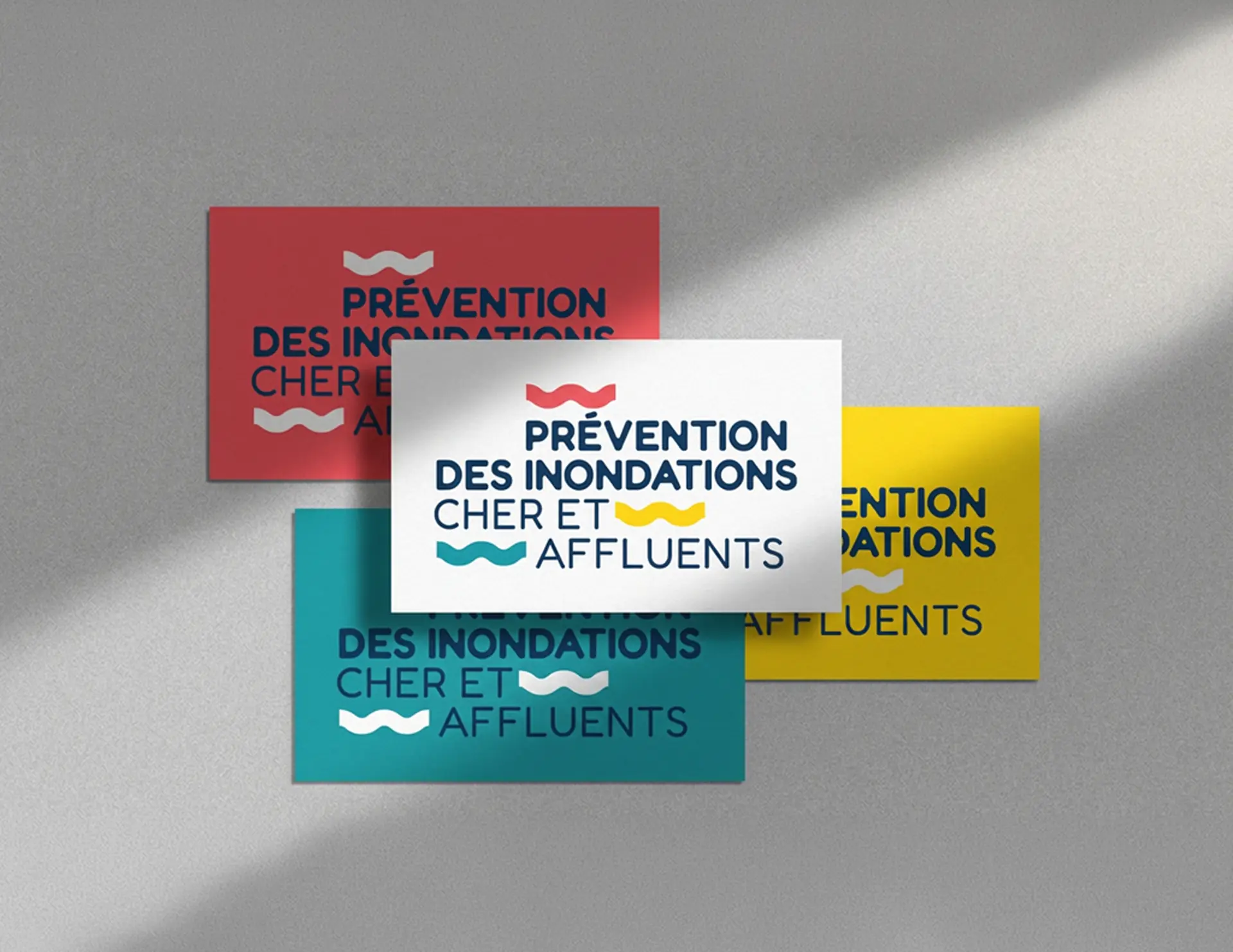 Quatre cartes de visite colorées (rouge, blanc, jaune, turquoise) superposées, affichant le texte 'Prévention des inondations Cher et affluents' avec des pictogrammes de vagues.