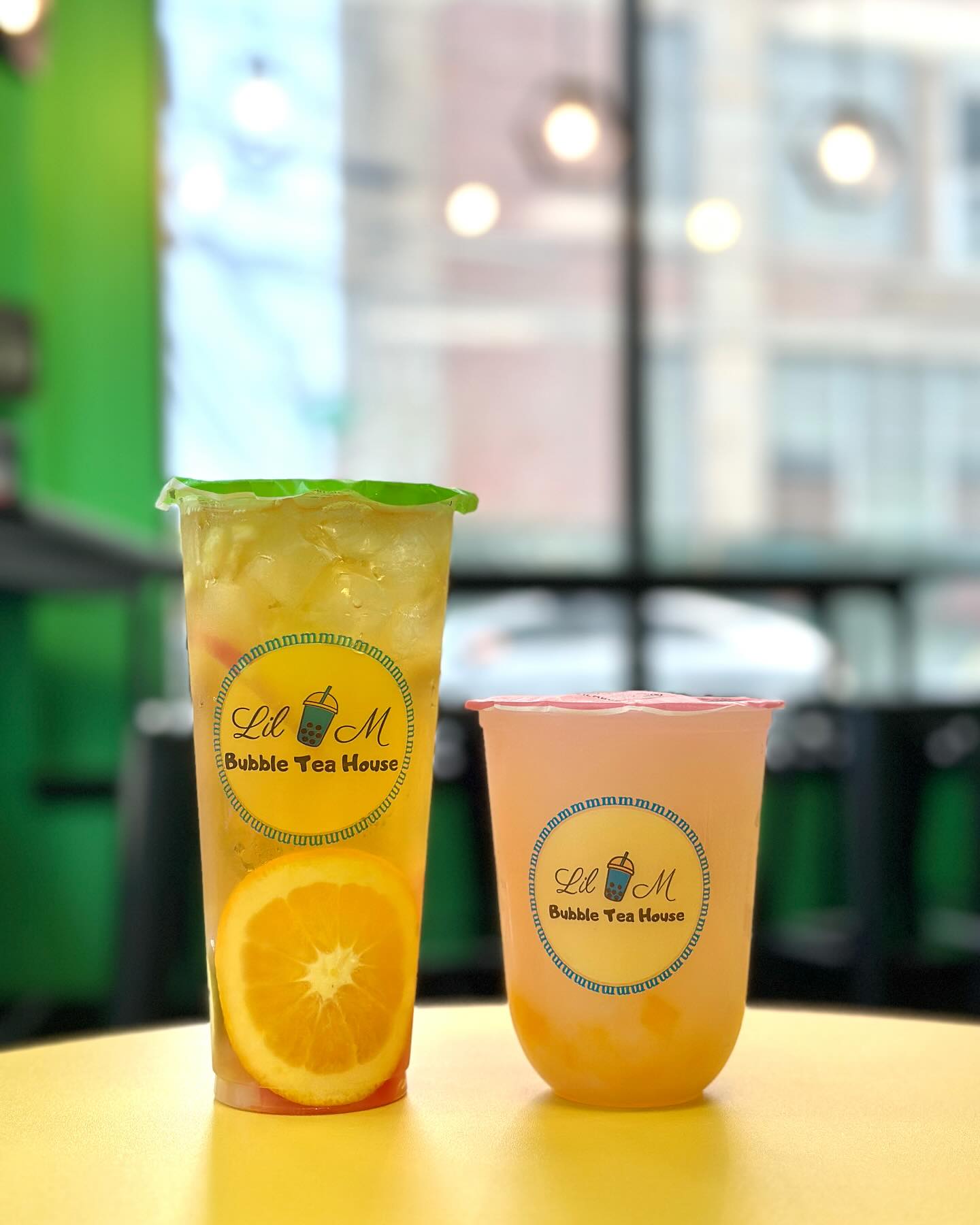 Two refreshing drinks from Lil M Bubble Tea: a citrusy orange tea with fresh orange slices and a light, fruity drink served in their signature cups, perfect for any bubble tea lover.