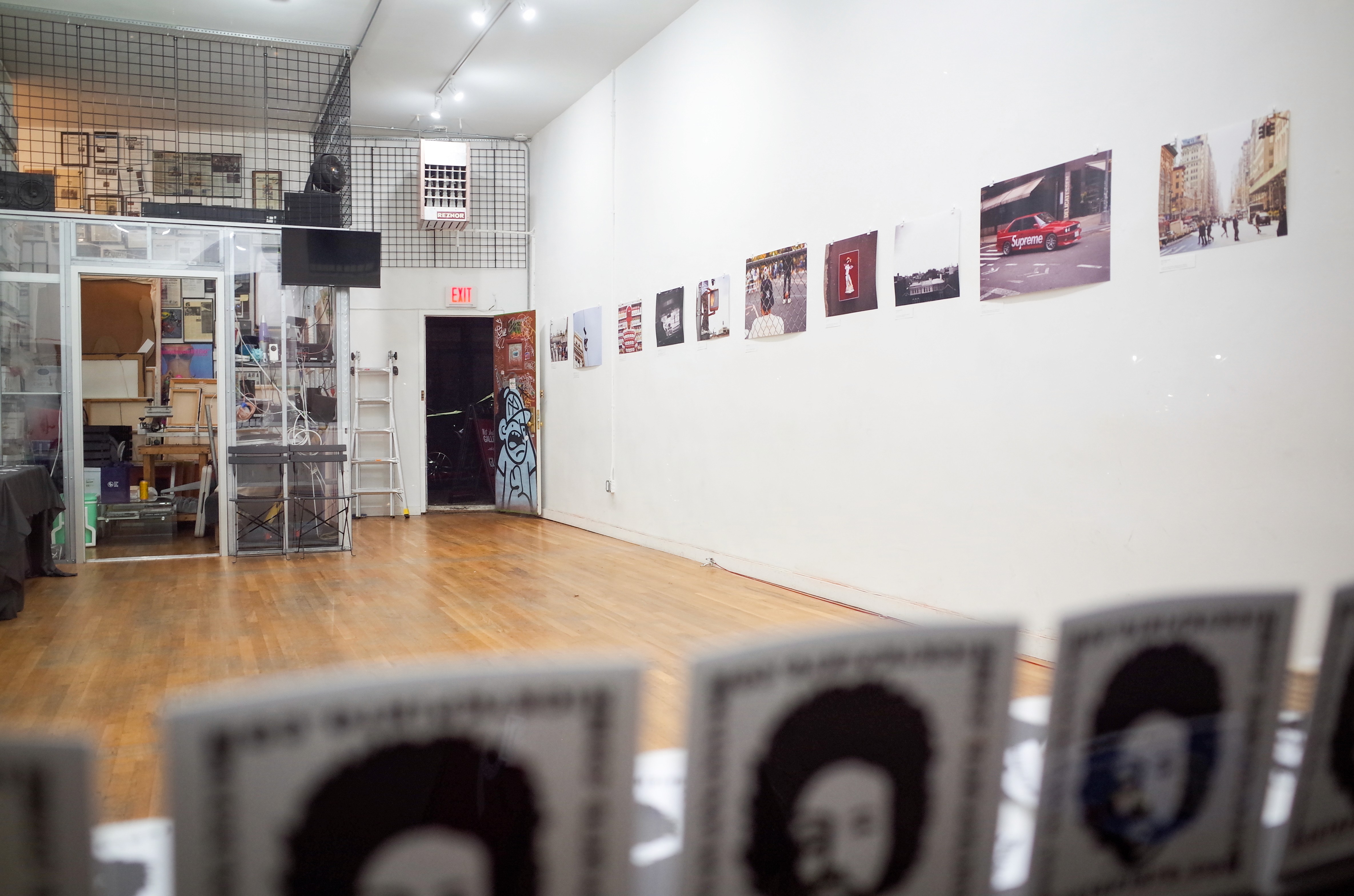 Wide interior view of the gallery with a long line of prints on the wall, with small cards in the foreground.