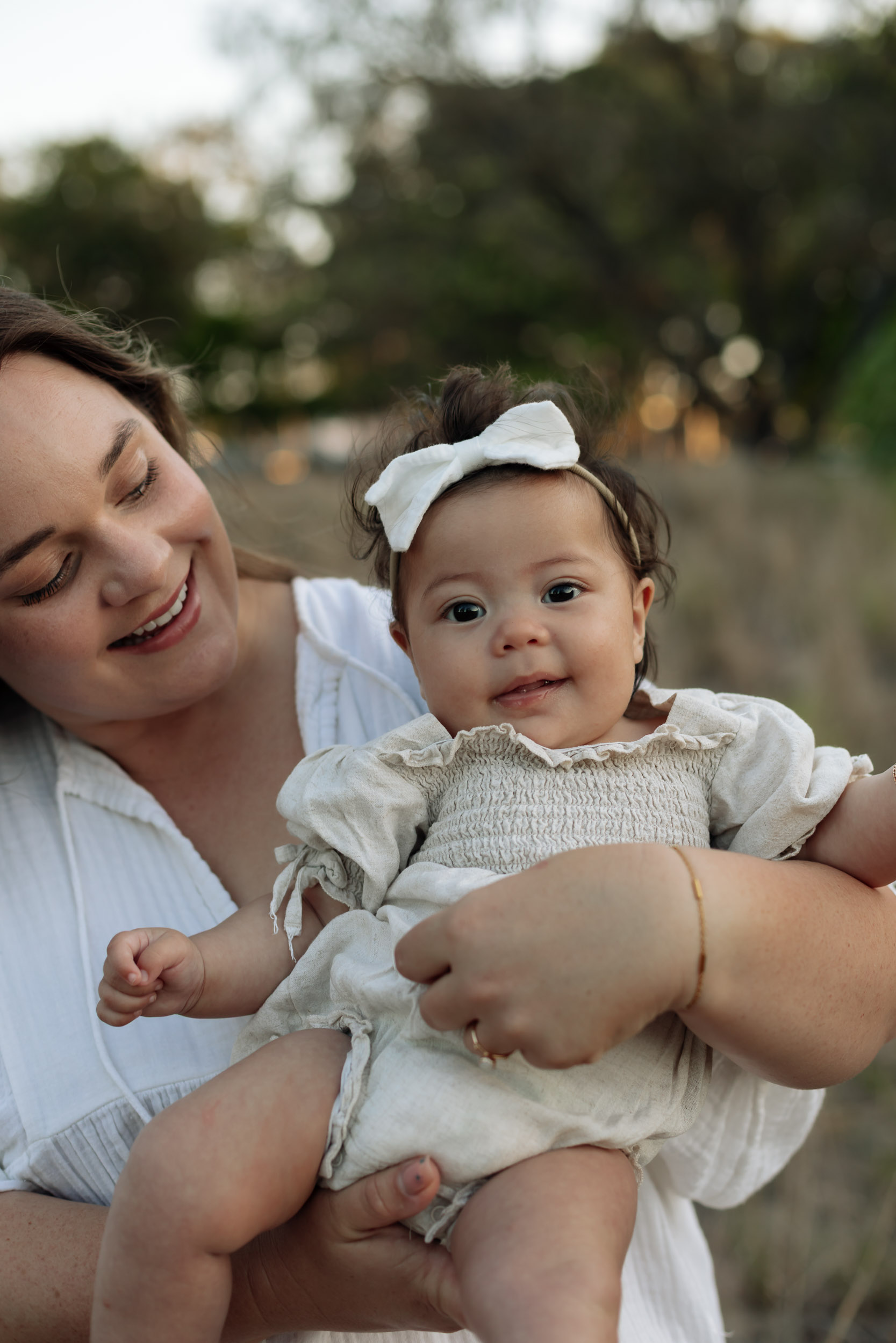 Natural light family photography in Mackay capturing mum and bub in a grassy field at sunset