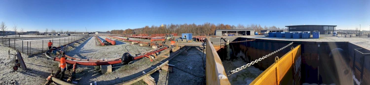Construction site with construction workers in the process of building infrastructure, red pipes, equipment, blue sky.