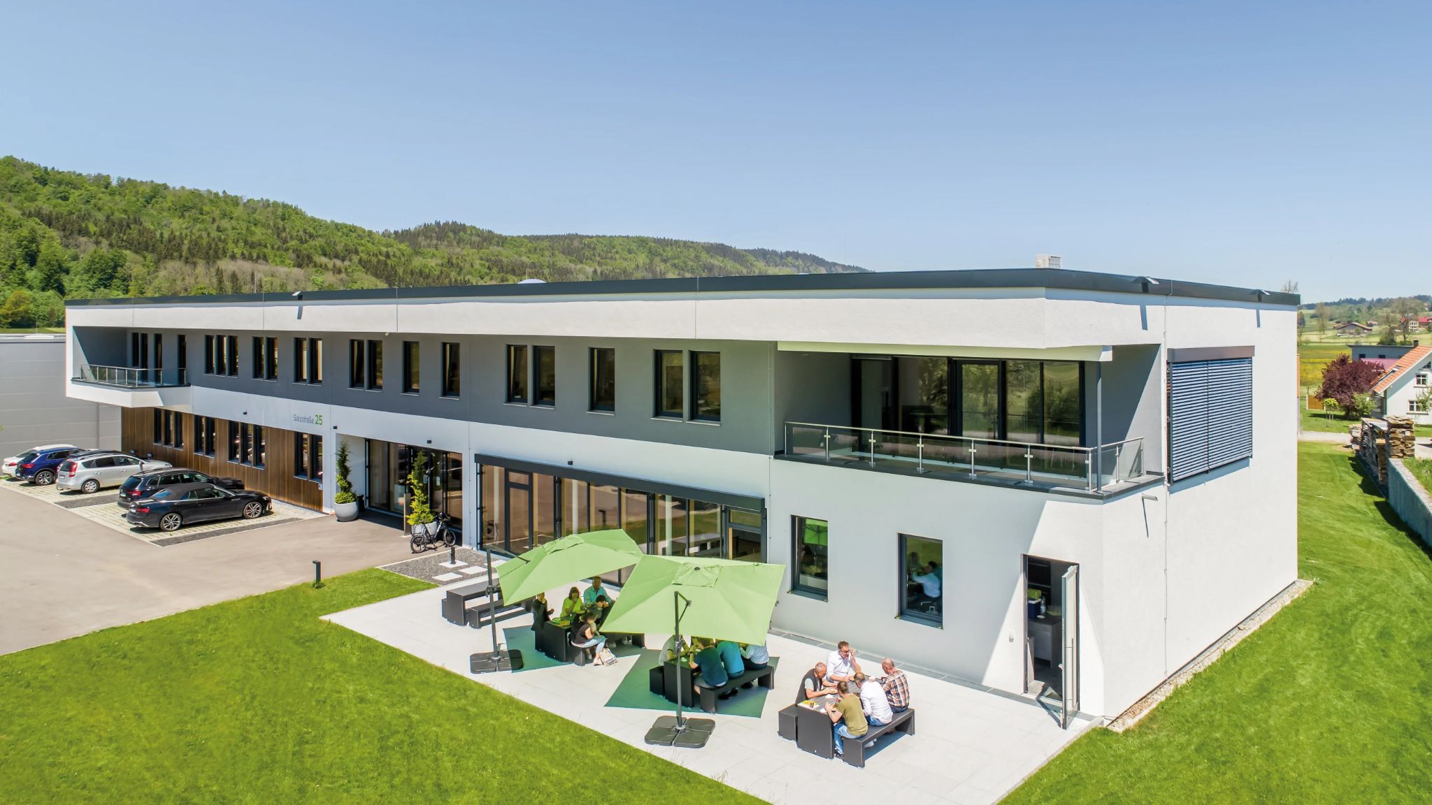 Blick auf modernes Bürogebäude mit Parkplatz und Terrasse davor.
