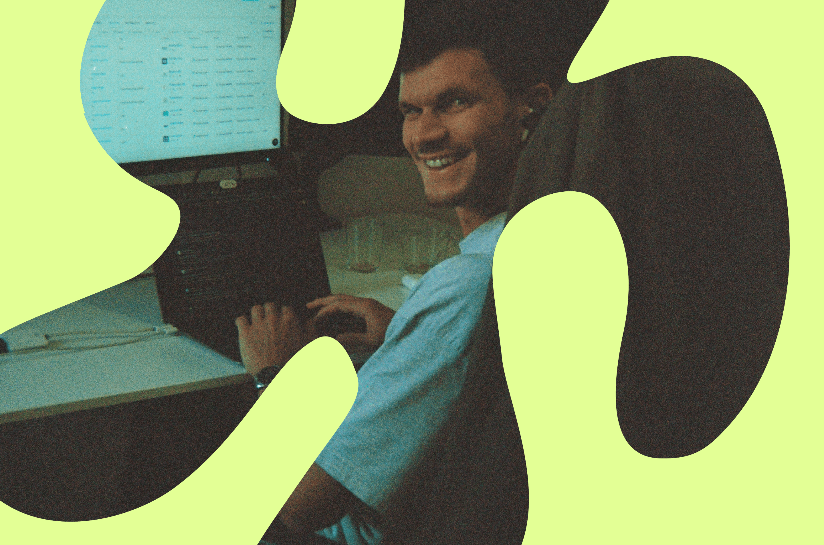 Smiling man working at a desktop computer in an office setting, partially framed by abstract light green graphic shapes overlaying the image.