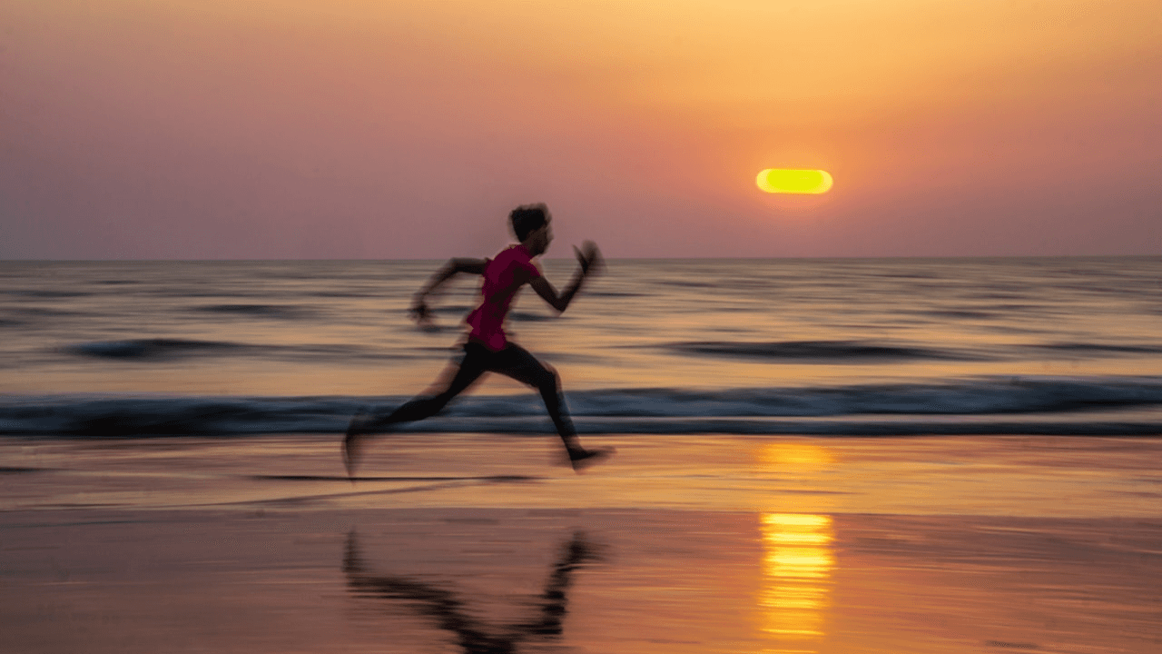 man running on beach with ocean and sunset in background