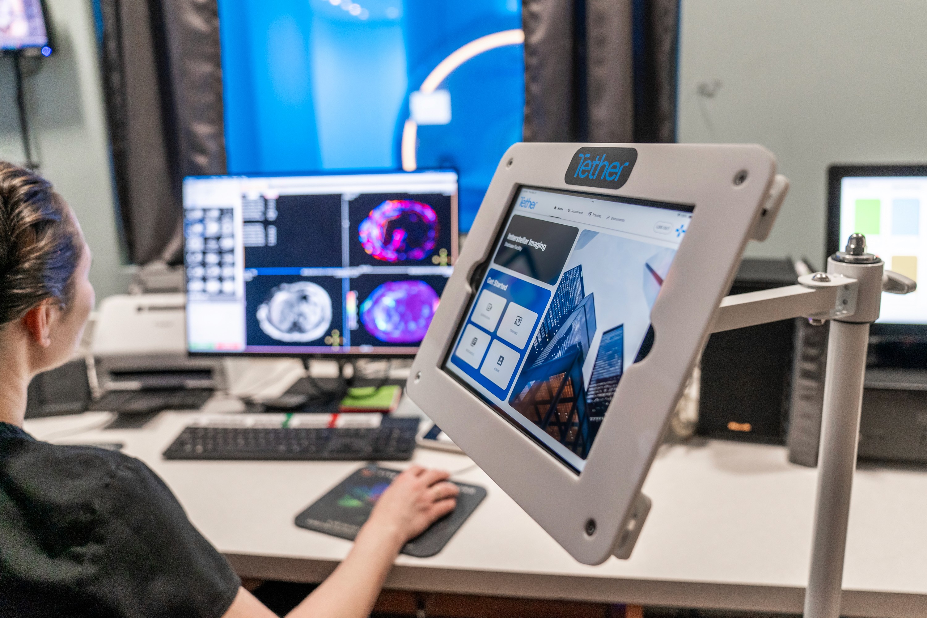 Radiology technologist operating CT imaging consoles alongside a Tether Supervision virtual contrast supervision unit, providing real-time radiologist oversight for safe, compliant contrast administration in outpatient imaging centers.