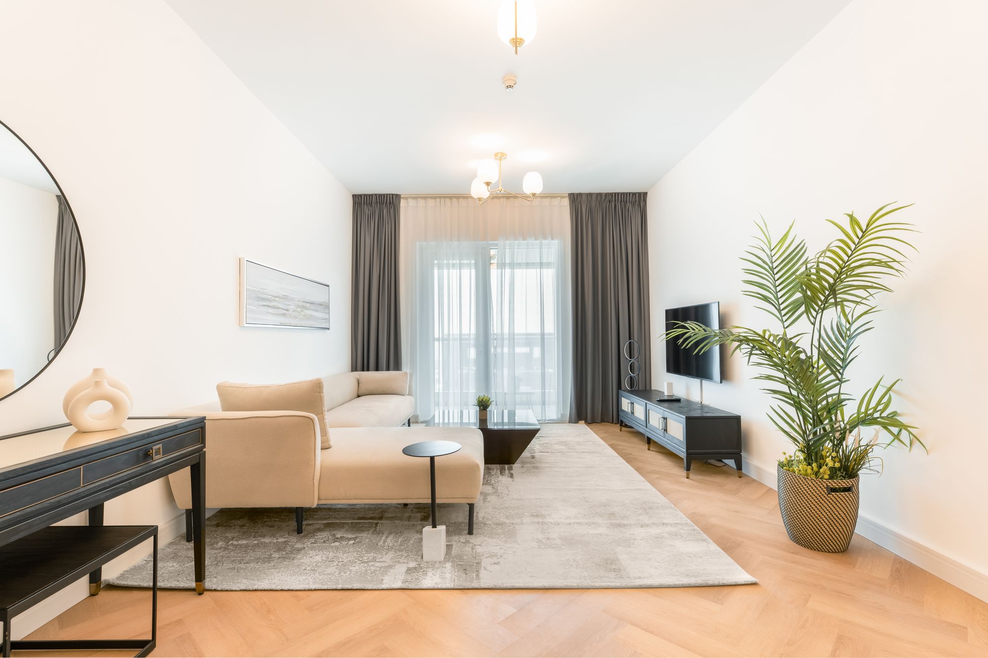 Un salon lumineux avec canapé beige, parquet clair et grande plante verte.