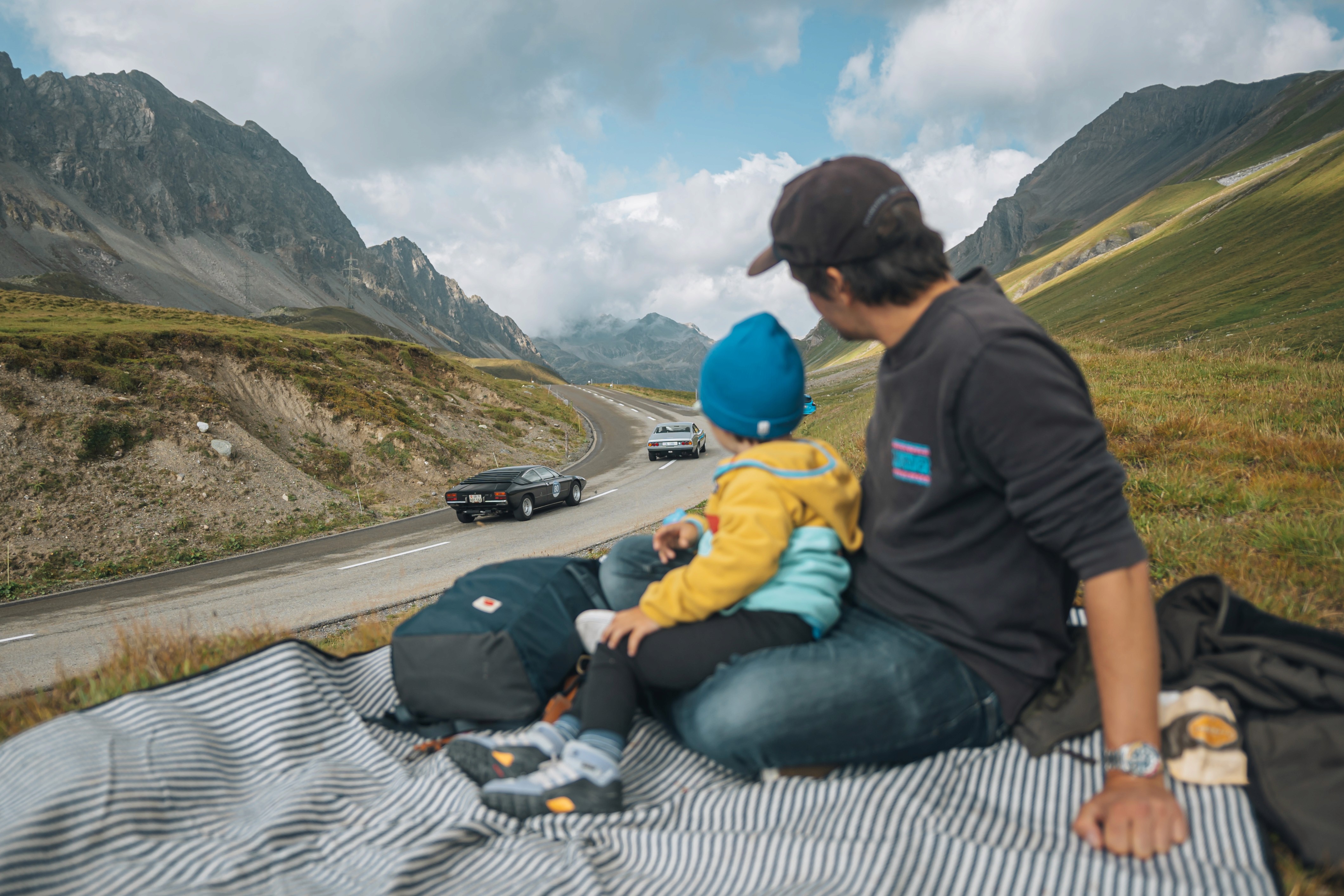 padre e figlio guardano gara di auto classiche con panorama montagna