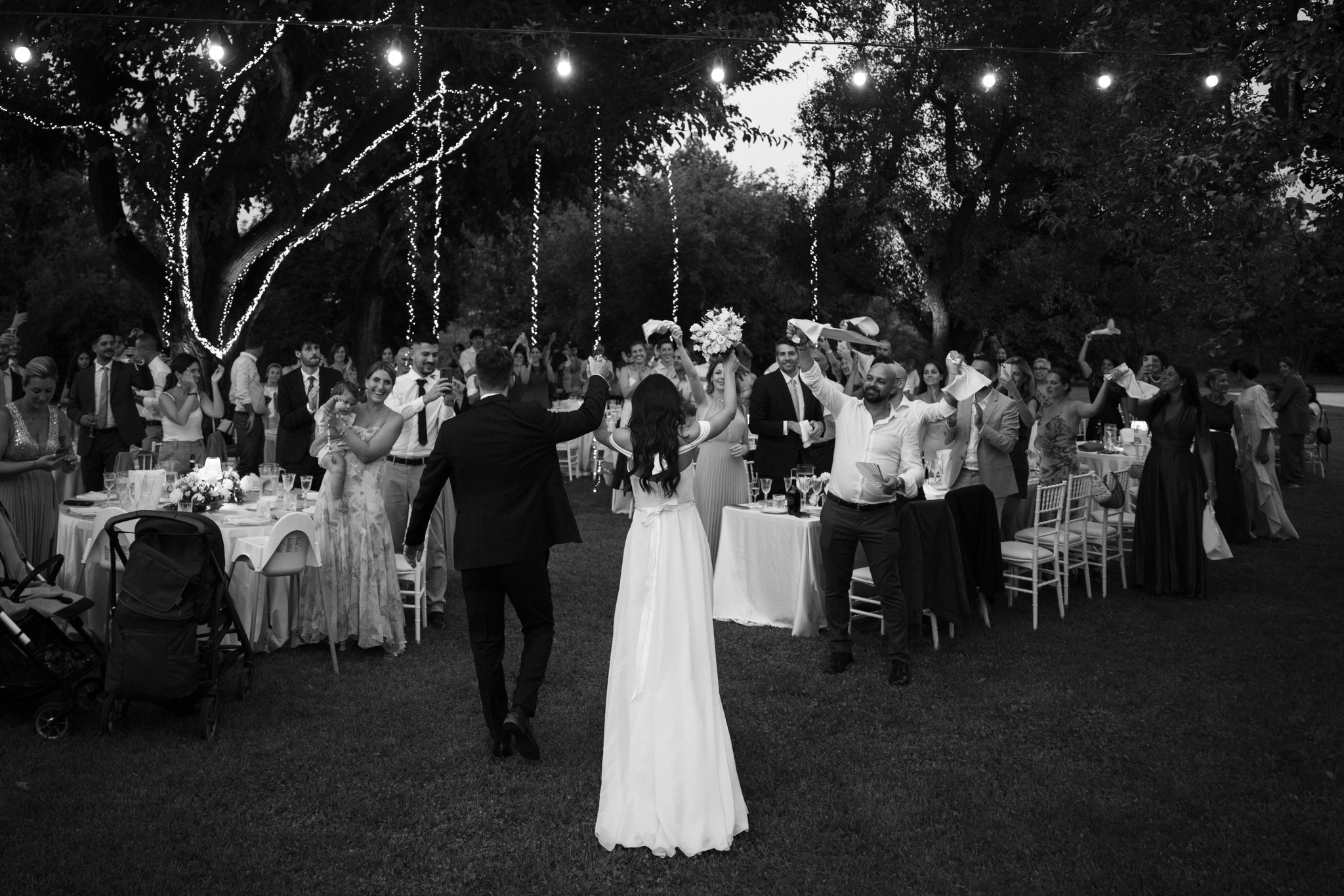 Sposa in abito bianco tra i tavoli del ricevimento notturno a Villa Negri, alberi illuminati durante il matrimonio