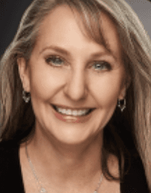 A smiling woman with long hair, wearing earrings, against a dark background. She has a warm and friendly expression.