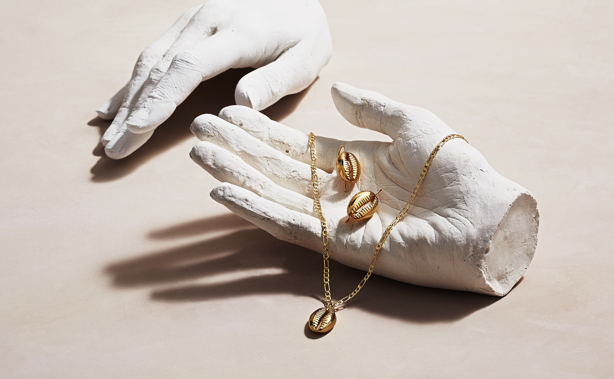 gold jewellery resting on an elegant hand sculpture, showcasing intricate details against a soft background.