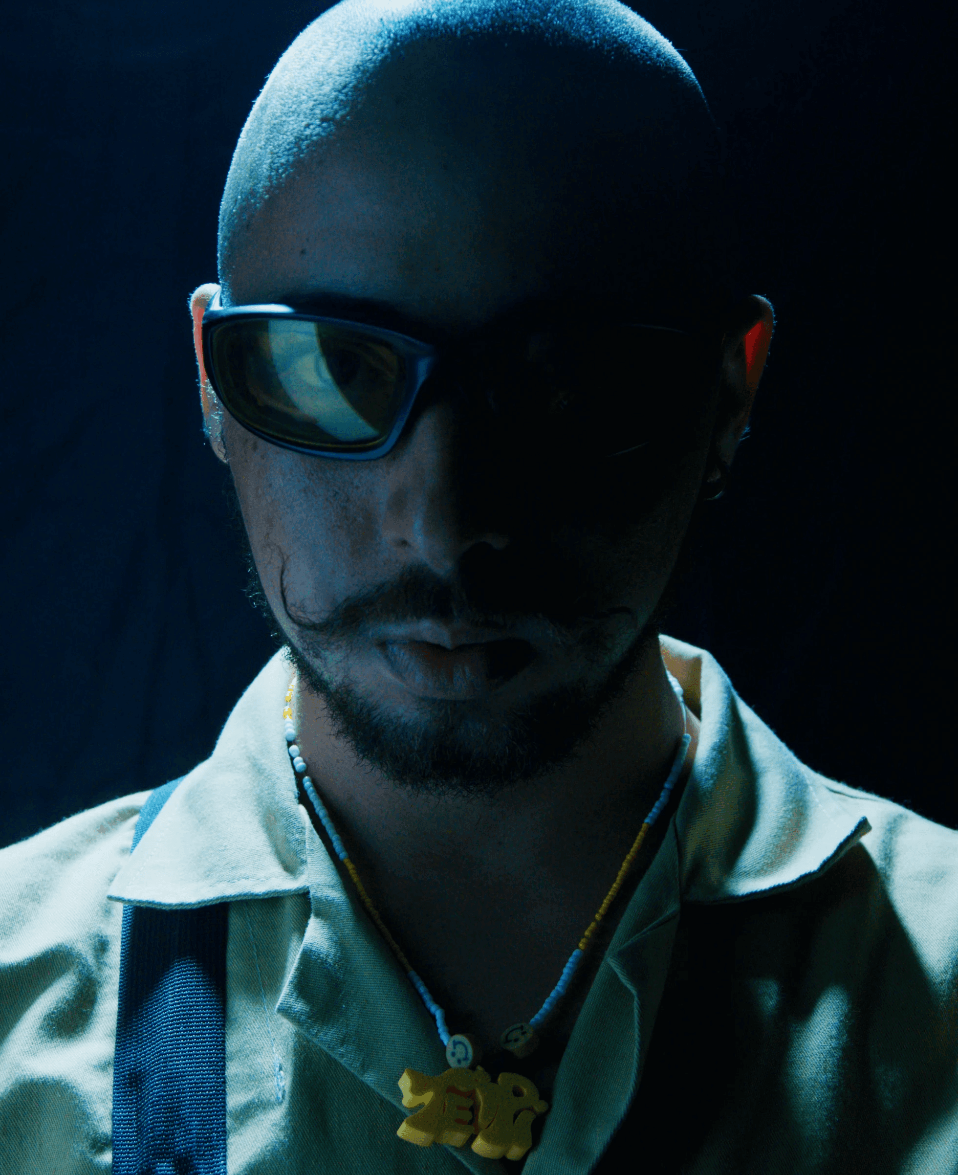Asian man with glasses in a creative workspace, surrounded by colorful abstract art and stationery on a cluttered desk.