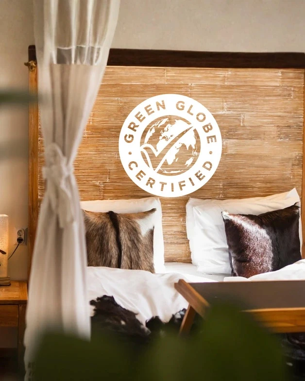 Hotel bedroom with wooden headboard, soft textiles, and Green Globe certification logo displayed