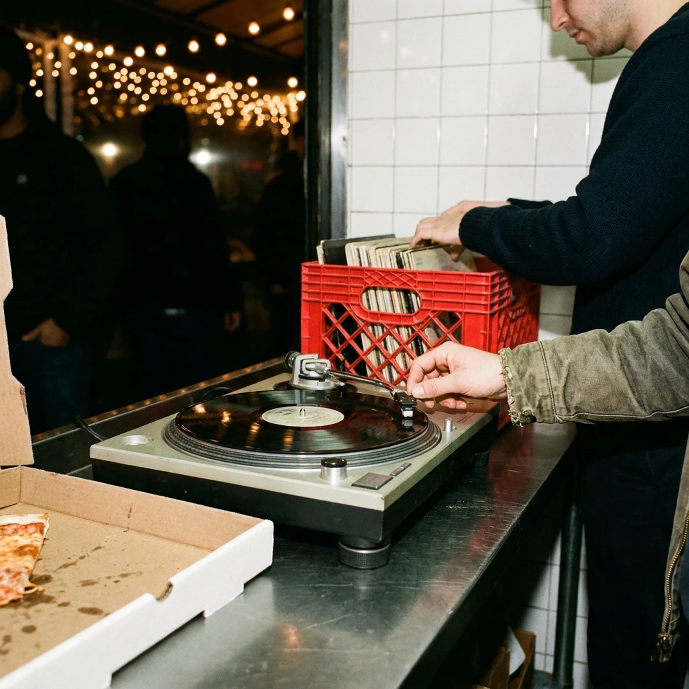 A hand cueing a record on a turntable beside an open pizza box