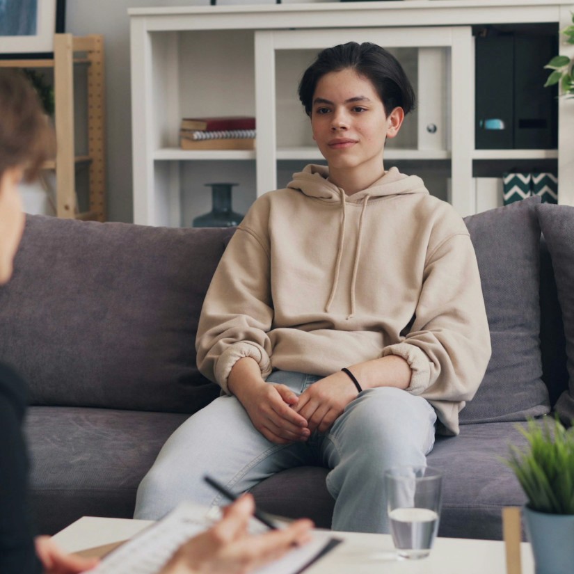 teenage boy in a hoodie, sitting on a couch in therapy session