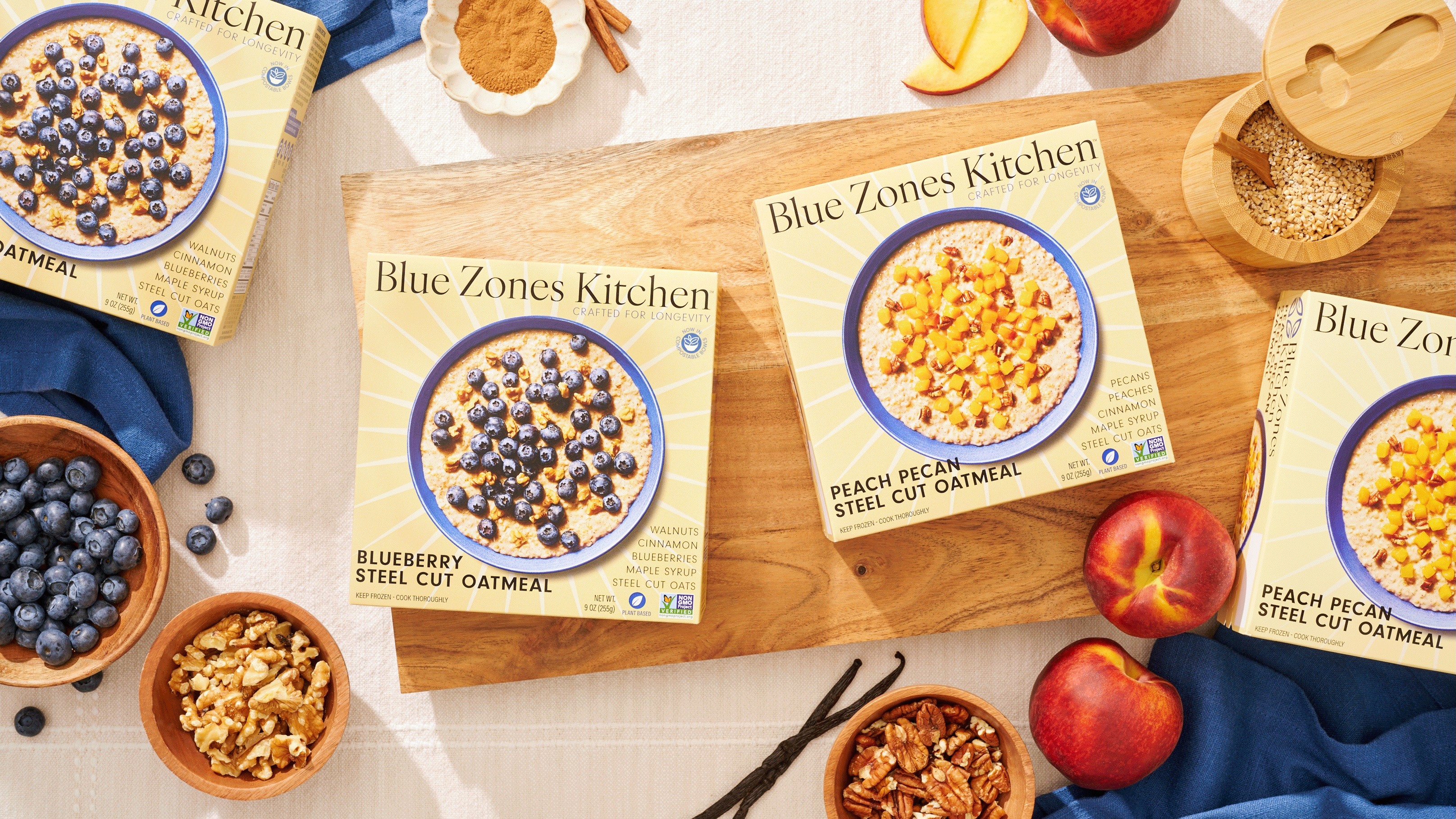 Blue Zones Kitchen oatmeal boxes displayed with fresh ingredients like blueberries, peaches, and nuts.