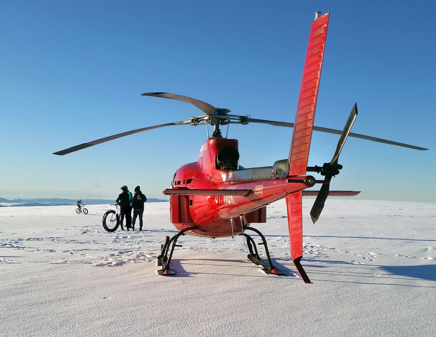 Helicopter in foreground with two men and bike on snowfield