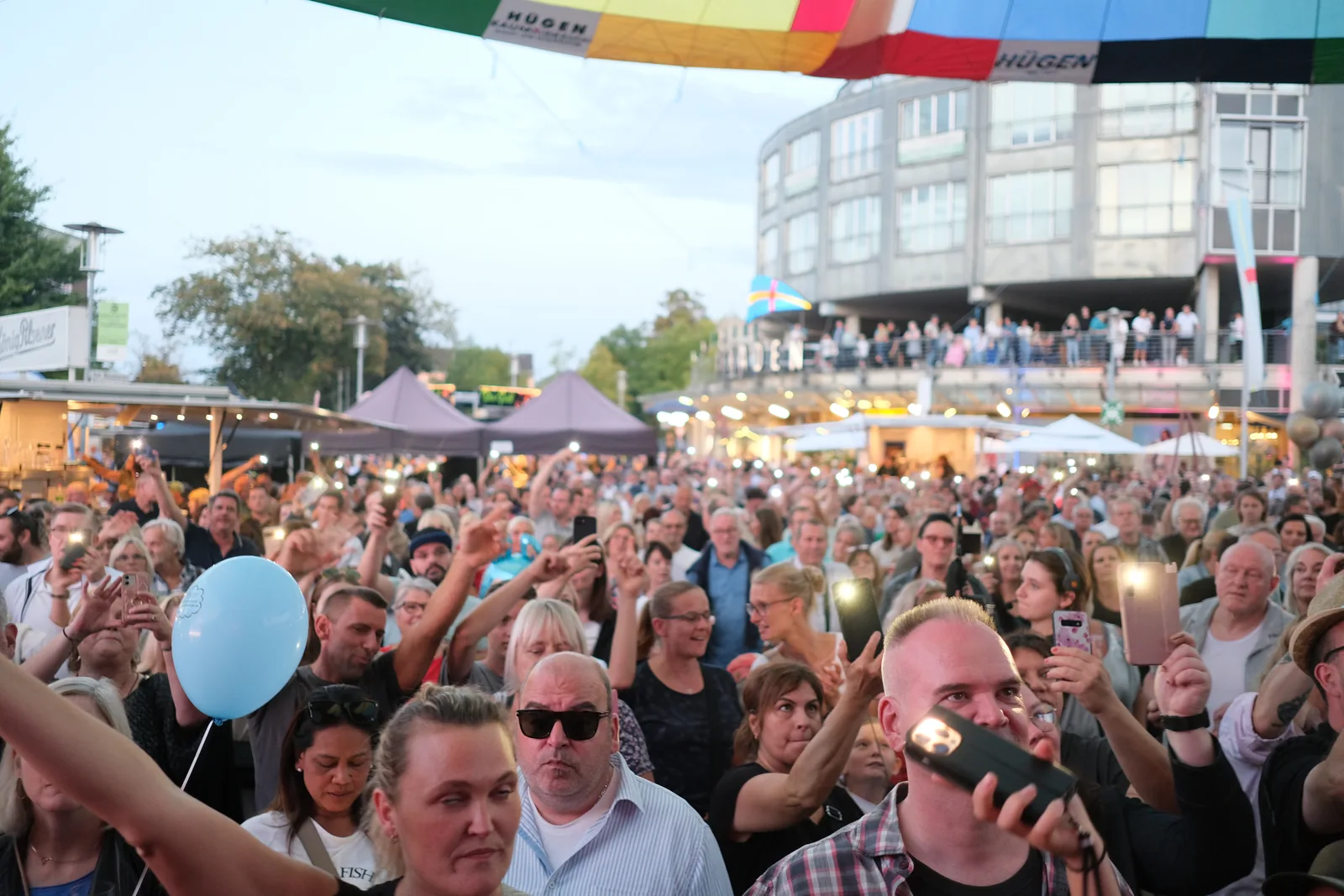 Publikum bei Tageslicht mit erhobenen Händen, ein Luftballon über der Menge.