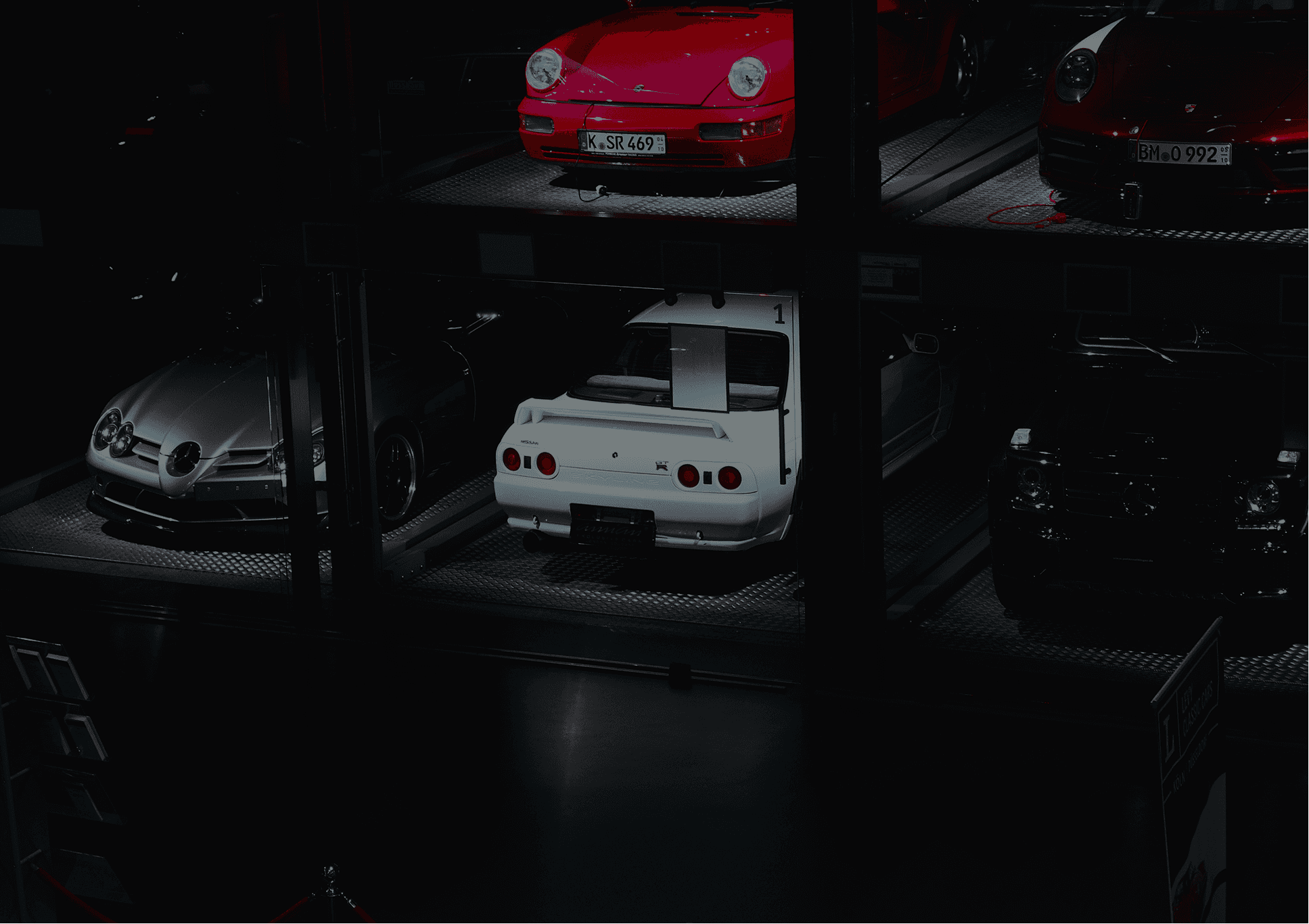 Moody lit storage area with cars on storage racks, rare mercedes, Nissan skylines, porsches etc