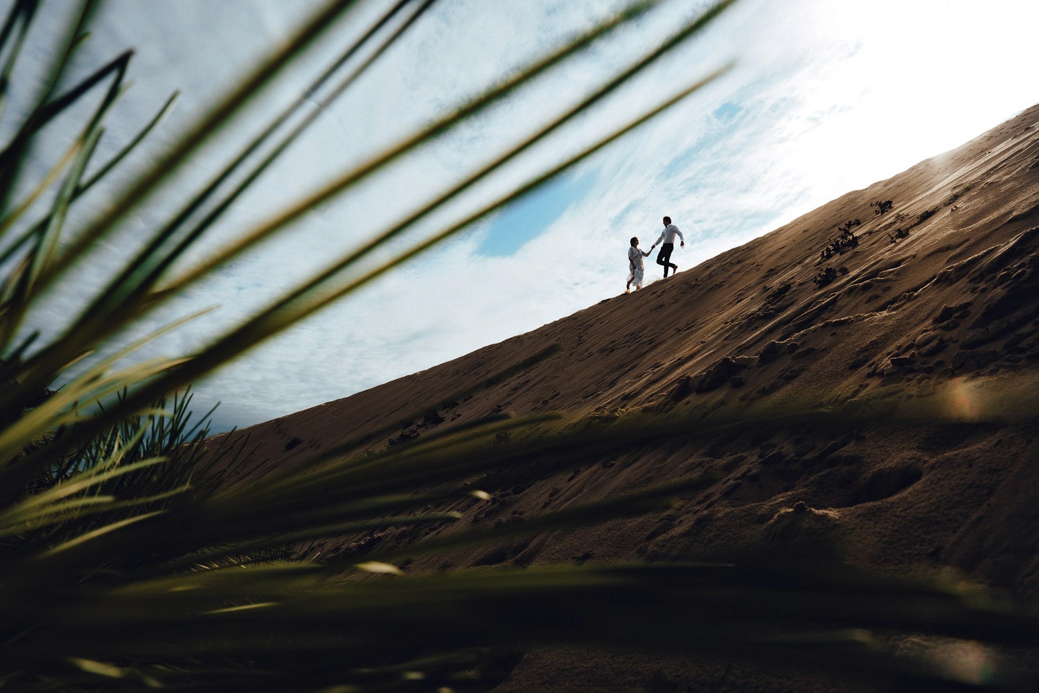 un couple marche sur une dune a seignosse entre sable et foret des landes lors d'une seance photo d'engagement