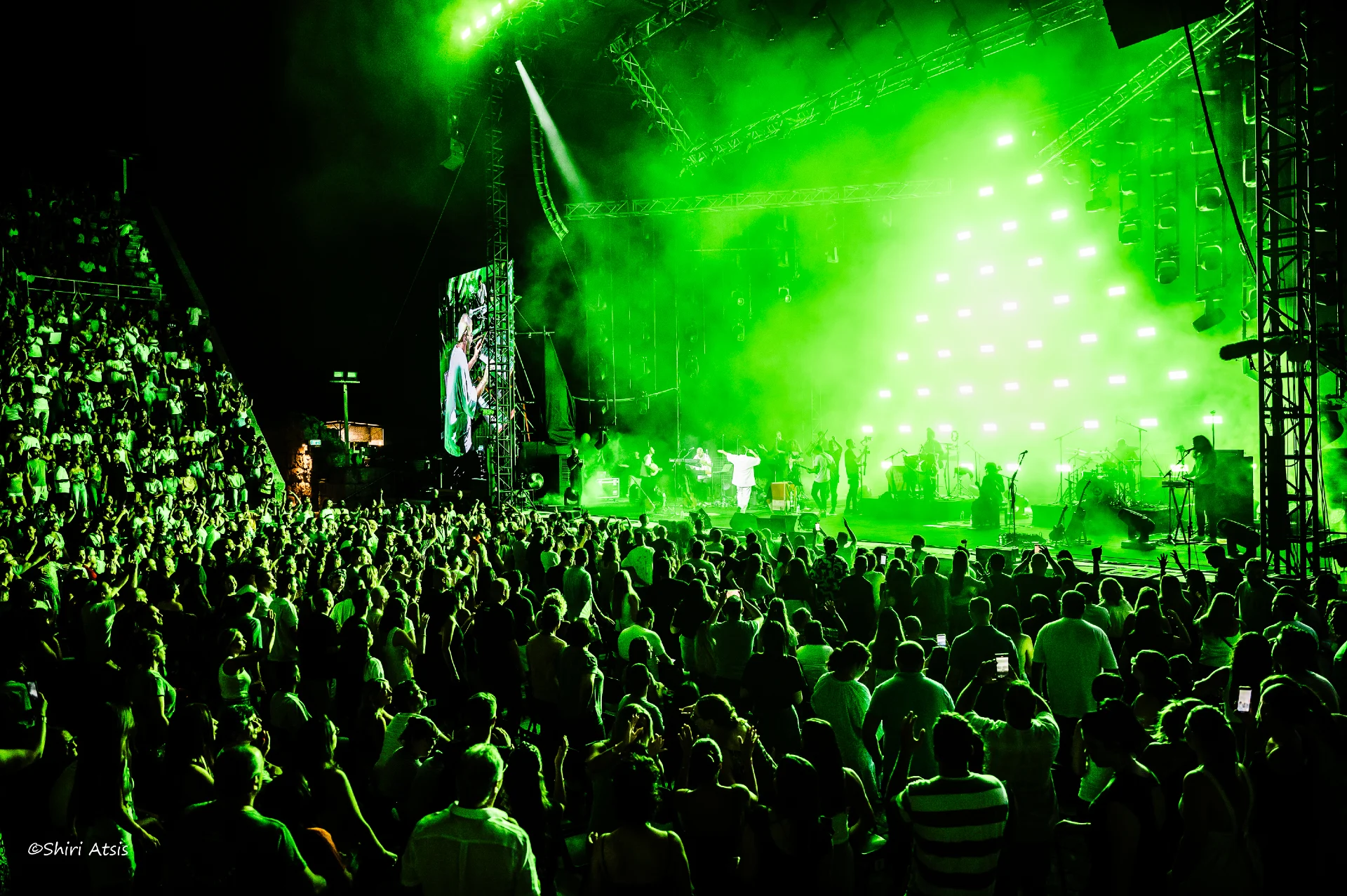 צילום פנורמי מרהיב מהופעה חיה של בניה ברבי. הקהל הרב ממלא את האמפיתיאטרון תחת תאורה ירוקה עוצמתית המוקרנת מהבמה ויוצרת אווירה מחשמלת, מאת Shiriz Photography הצלמת שירי עציץ.