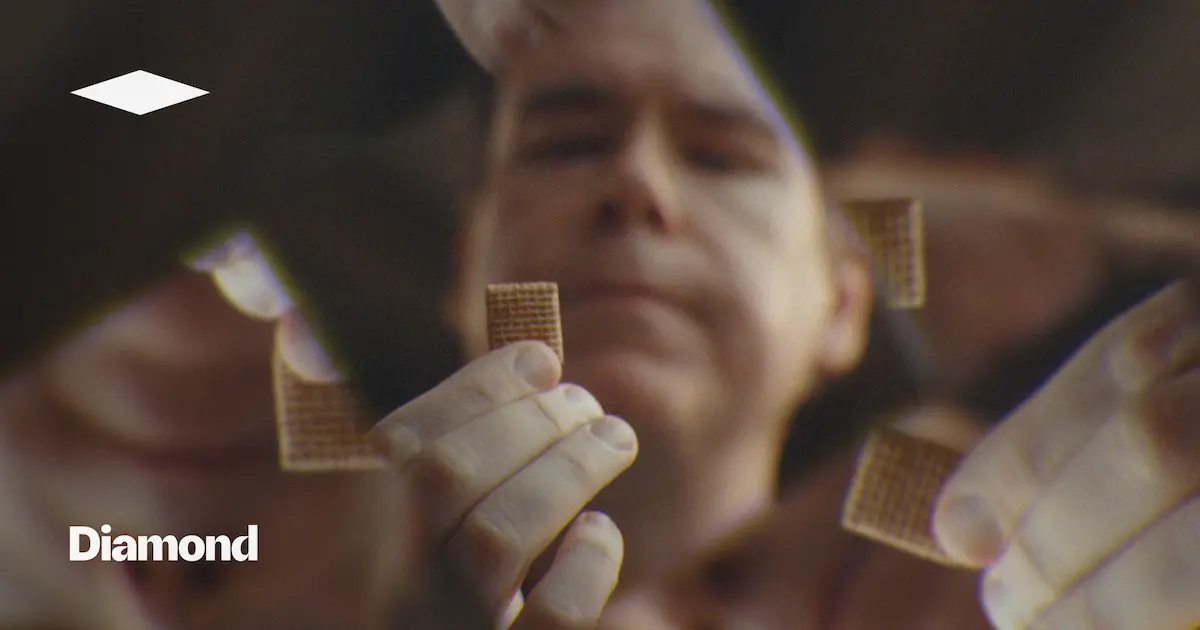 A person holding a piece of shredded wheat in their hand