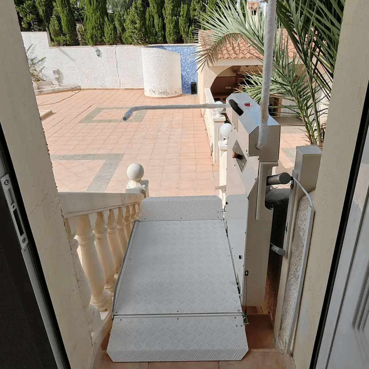 An outdoor inclined platform lift installed on external steps at a residential property, showing the open folded platform and track mechanism mounted to the staircase wall.