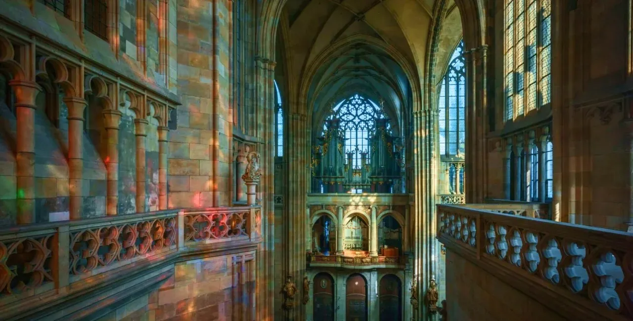 Gothic cathedral interior with stained glass light and vaulted arches.