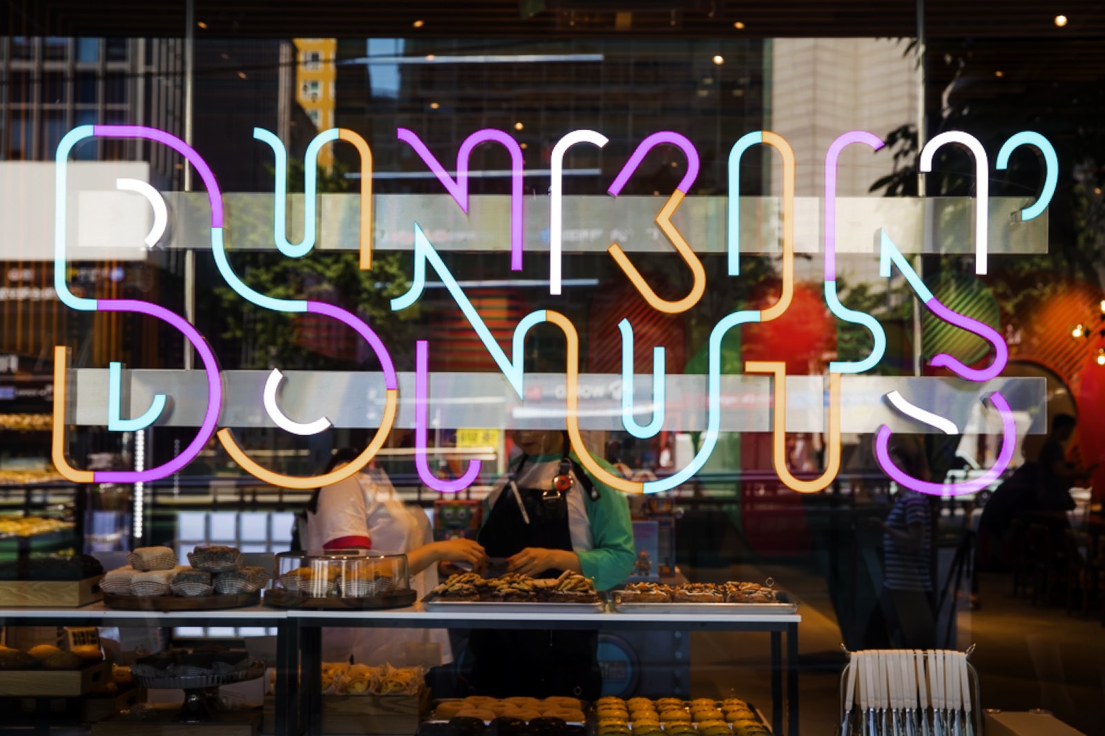 A vibrant neon sign spelling "Dunkin' Donuts" lit up against a colorful background of blurred lights and décor.