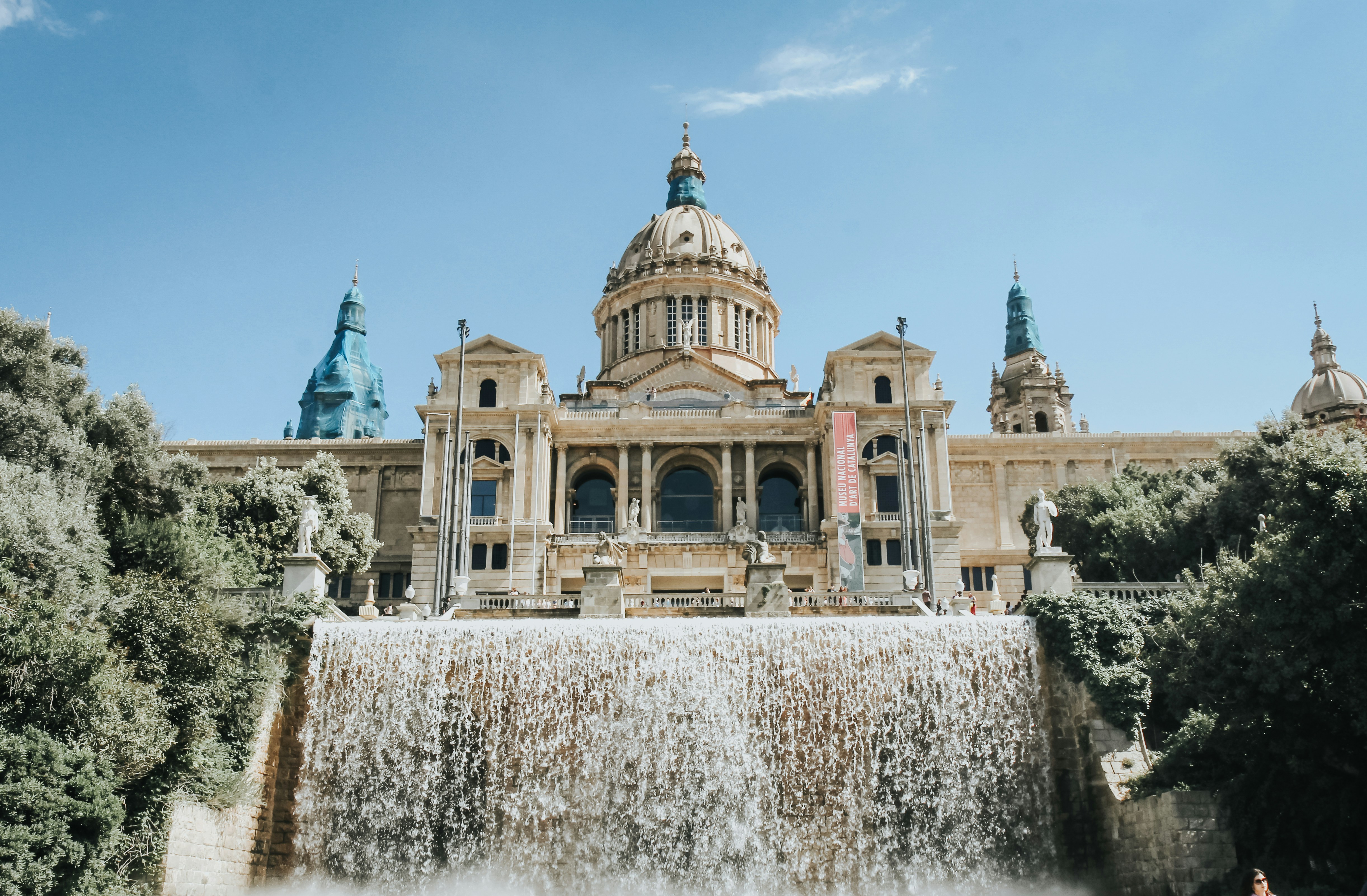 The dome of the Museu Nacional d'Art de Catalunya main building, with a waterfull from a large fountain pouring water at the forefront. 
