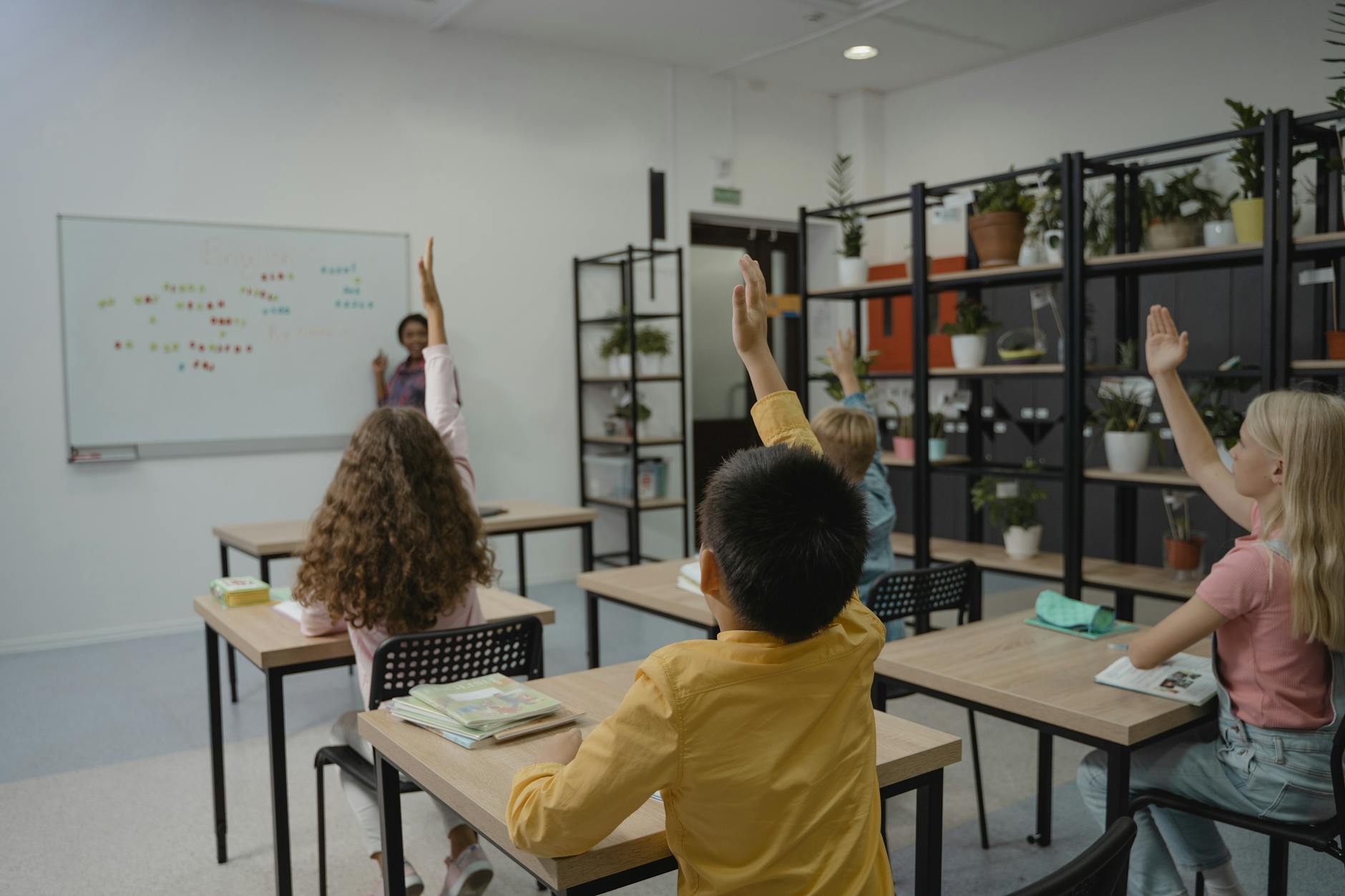 An elementary teacher stands at a large interactive whiteboard displaying a literacy game to an engaged classroom.