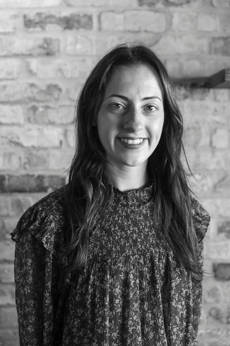 Jacqueline from Macchialina smiling warmly in front of a rustic brick wall.