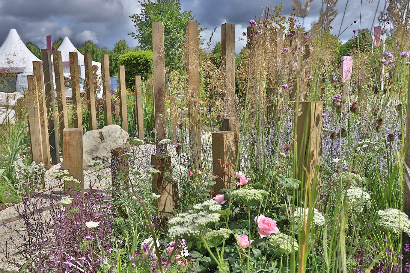 A lush garden featuring vibrant flowers, tall plants, and green foliage under a partly cloudy sky.