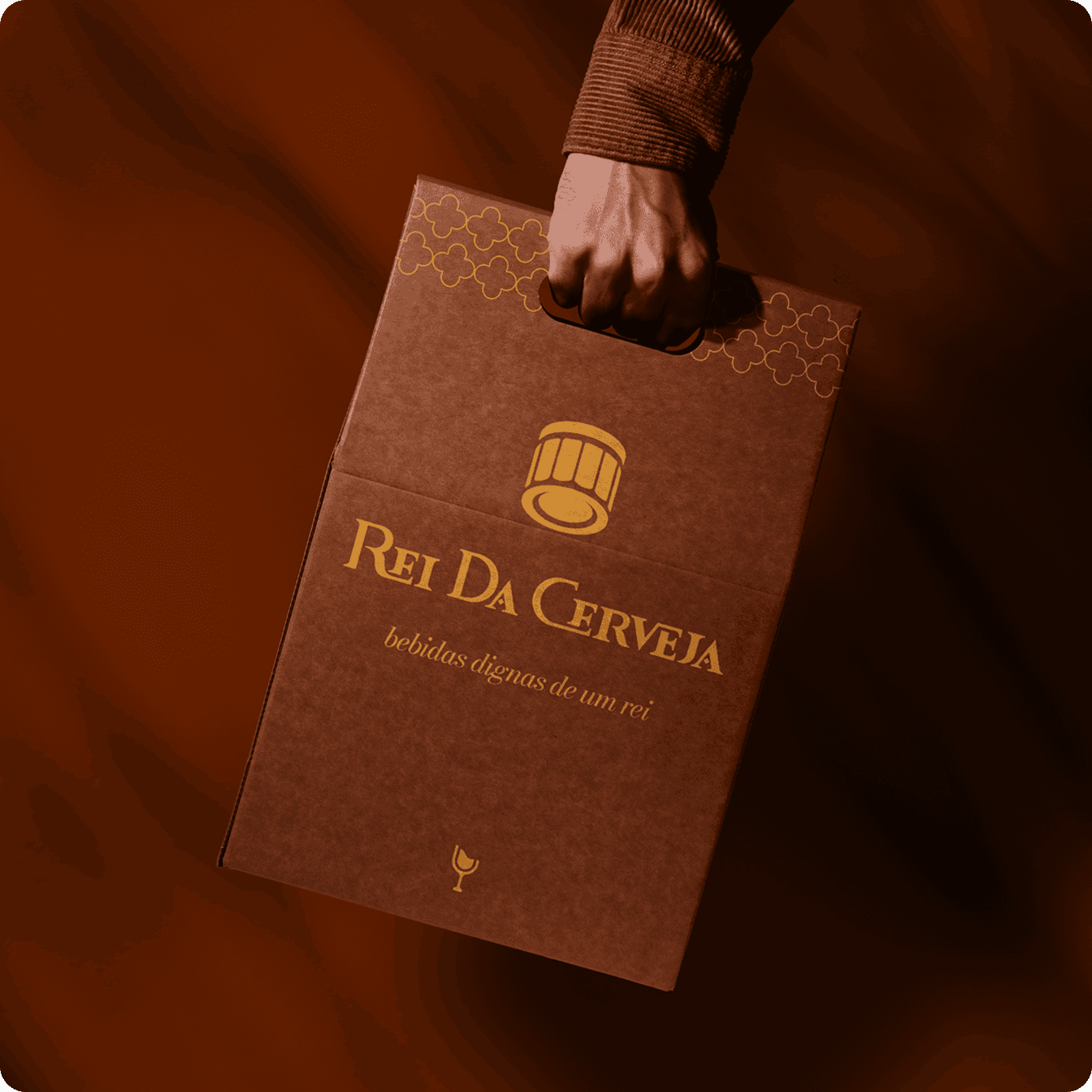 uma embalagem para transporte de vinho com design da marca Rei da Cerveja. A embalagem é marrom e possui os elementos da identidade visual em amarelo.