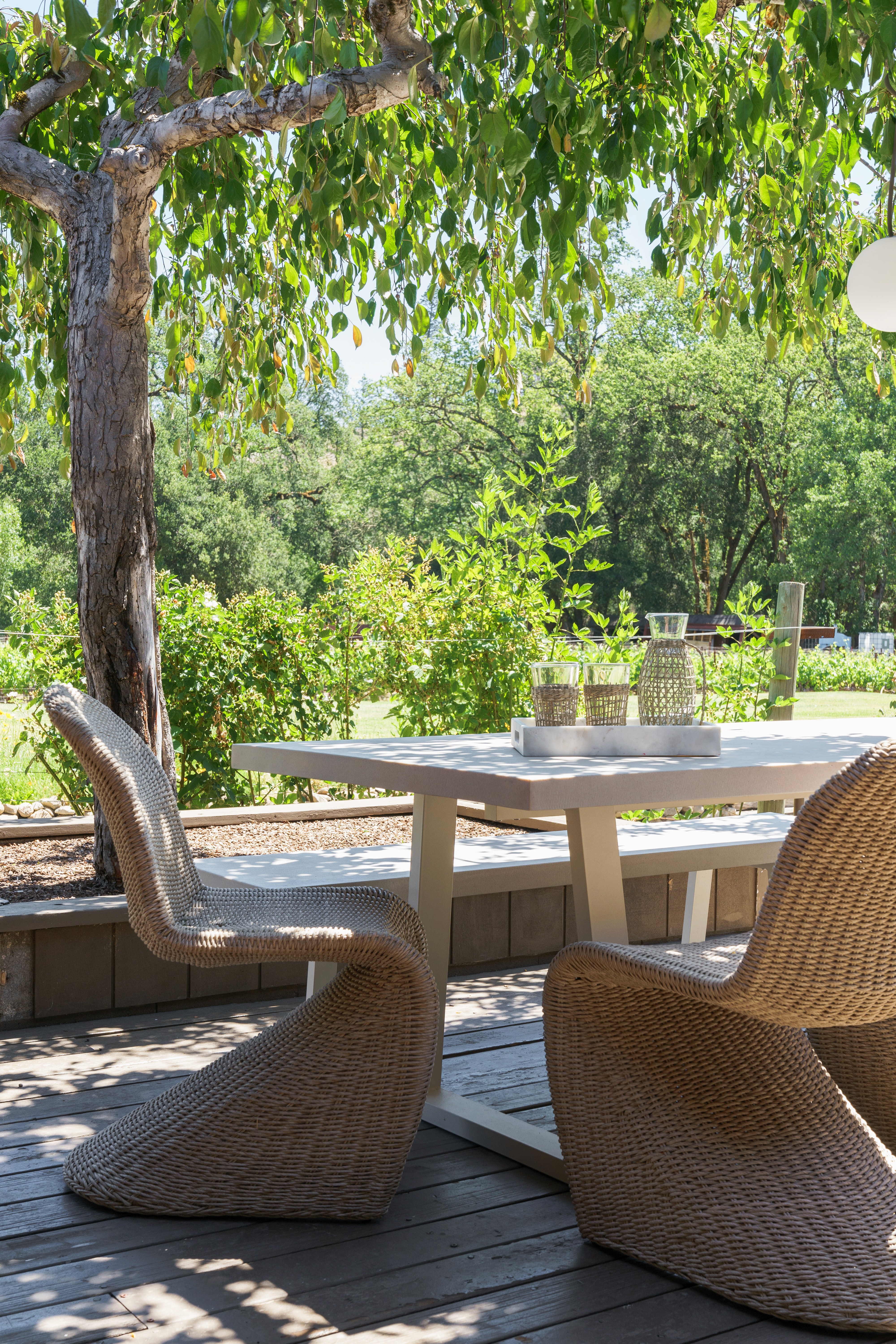 This outdoor living design blends modern luxury with nature, featuring a beach-club-style seating area, natural wood tones, lush greenery, and elegant pool stone accents for a tranquil retreat