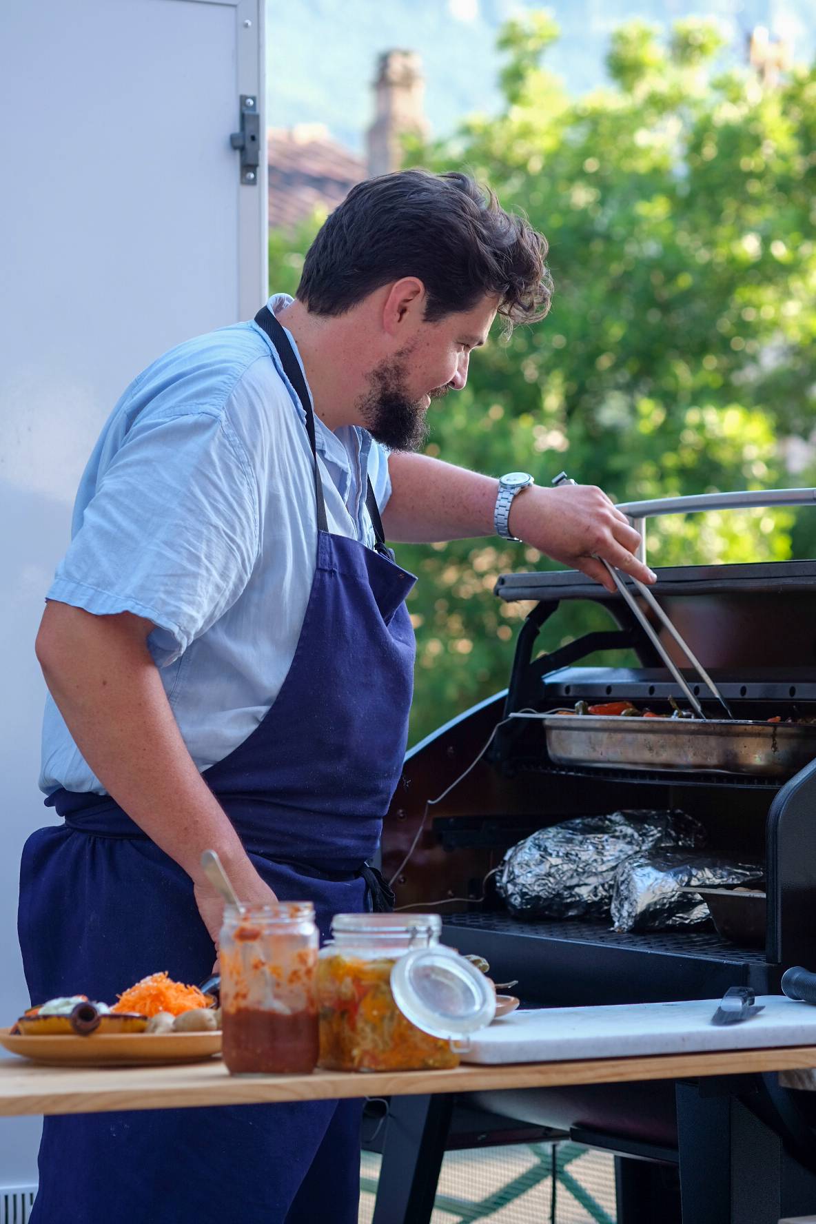 Chef traiteur en train de cuisiner au barbecue lors d’un événement extérieur avec produits frais.