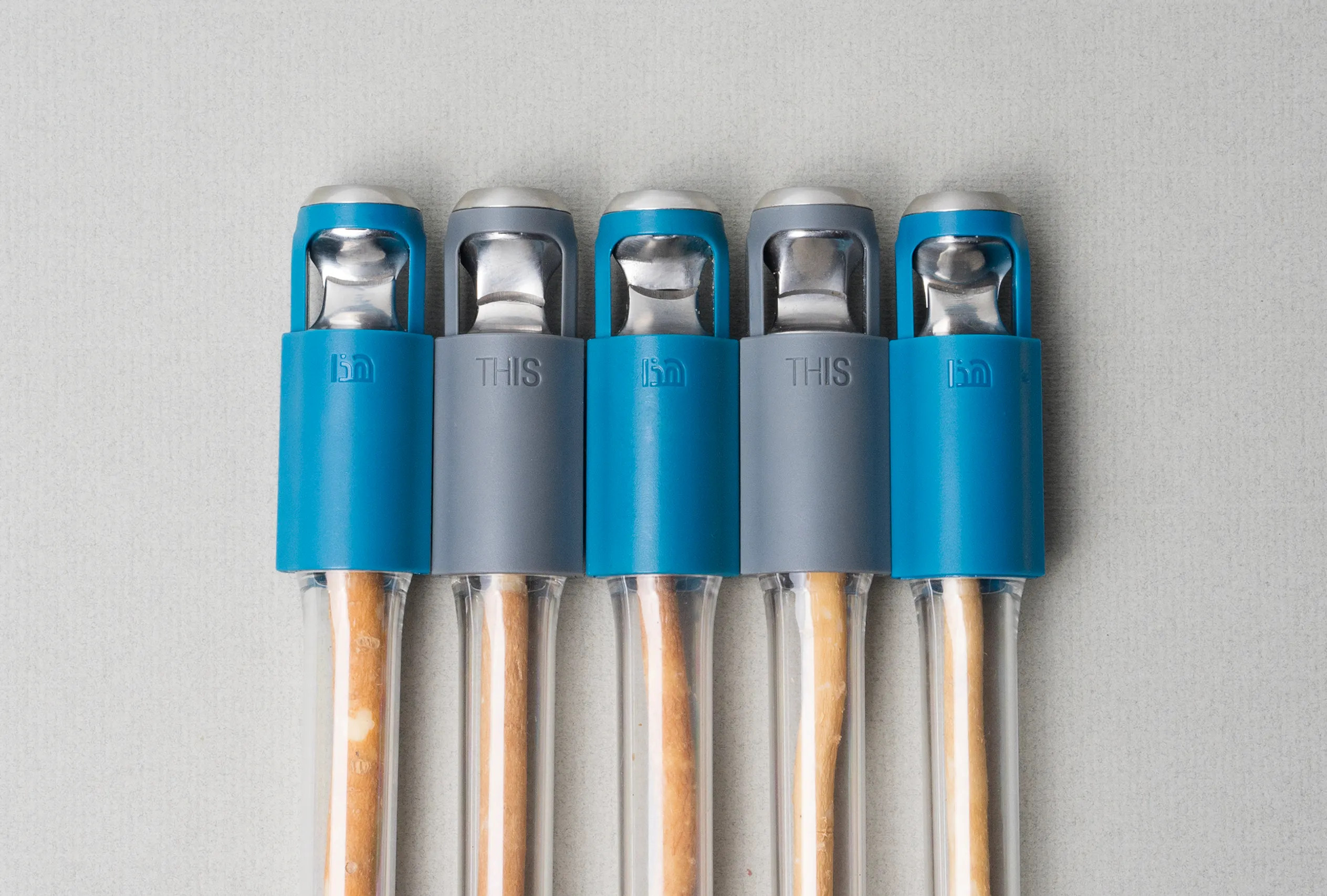 Five blue and gray THIS toothbrushes with natural miswak sticks arranged side by side