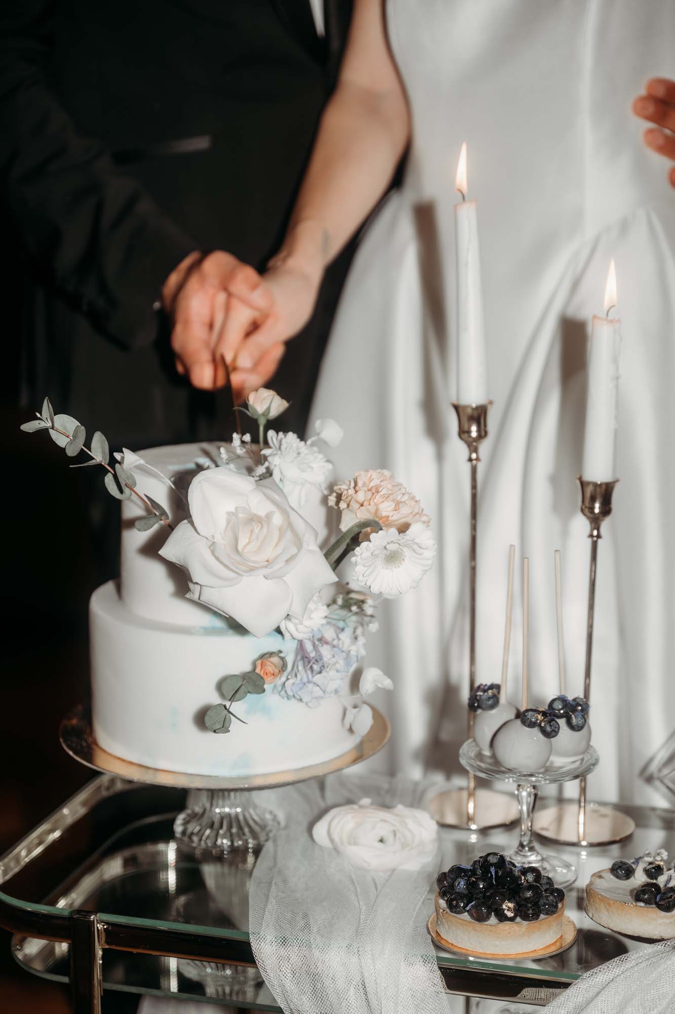 Tortenanschnitt einer Torte mit frischen Blumen, angerichtet auf einem Servierwagen mit Törtchen.