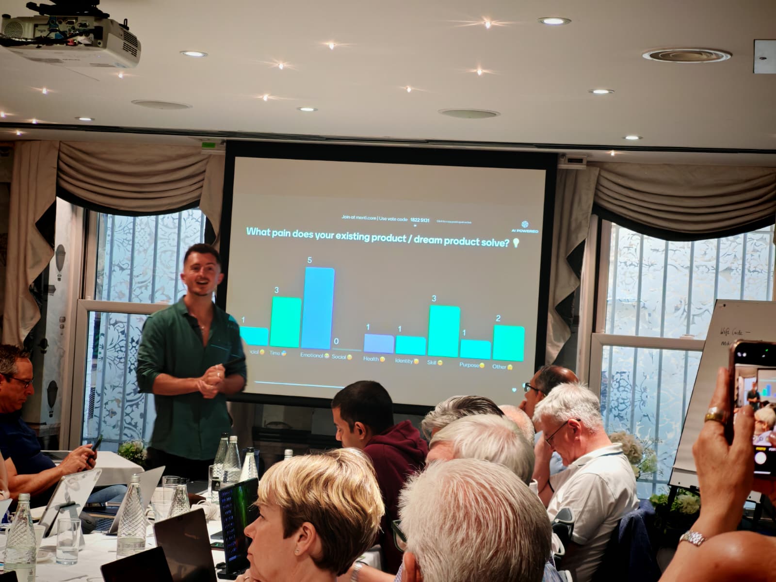 Cozy reading nook with sofa, chair, and plants inside a glass cabin with mountain forest views.