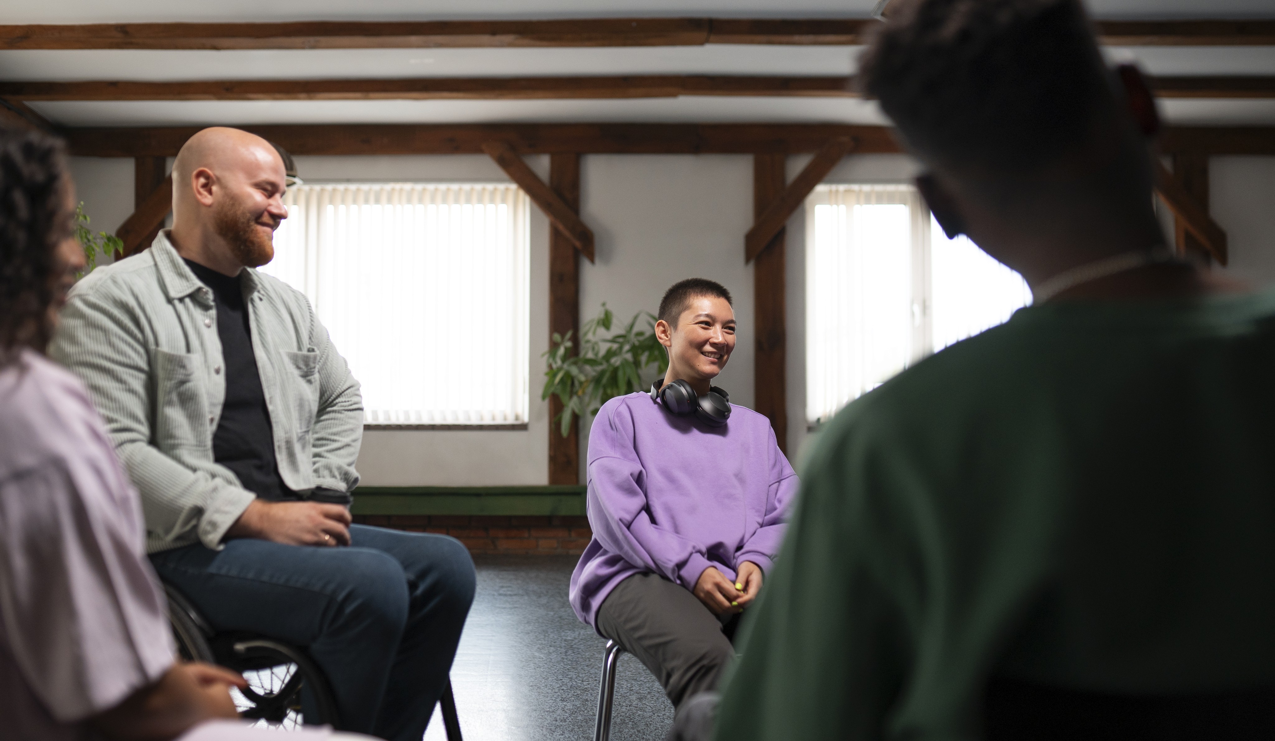 A smiling young man with crossed arms, wearing a plaid shirt and white t-shirt, poses against a dark background.