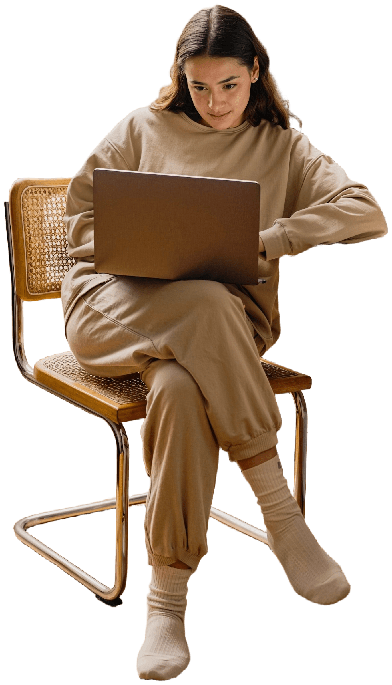 A person seated in a chair, focused on a laptop, wearing a tan outfit. Soft lighting highlights the scene.