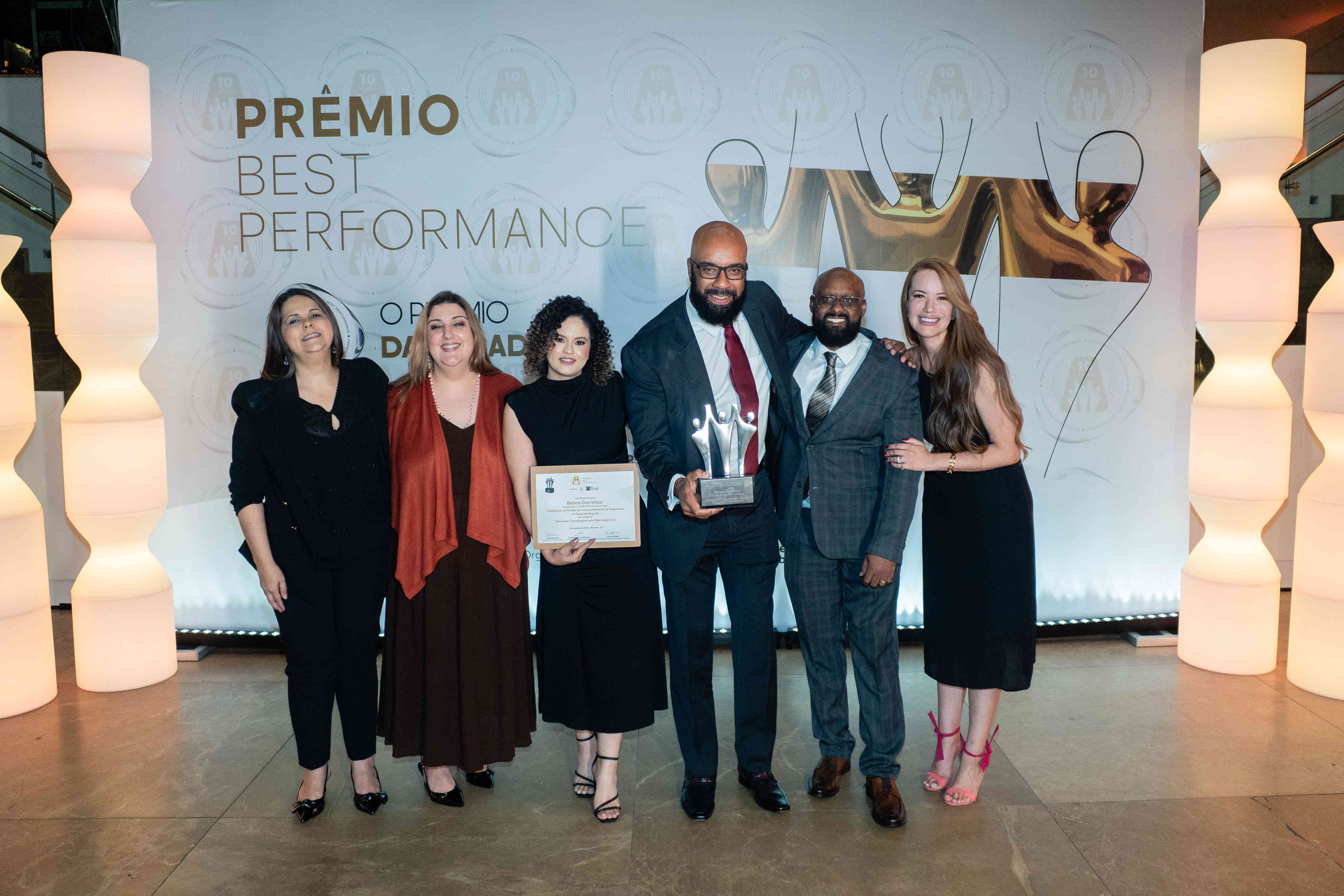 Executivos do Banco Carrefour posando com troféu prata e certificado no palco do Prêmio Best Performance 2025