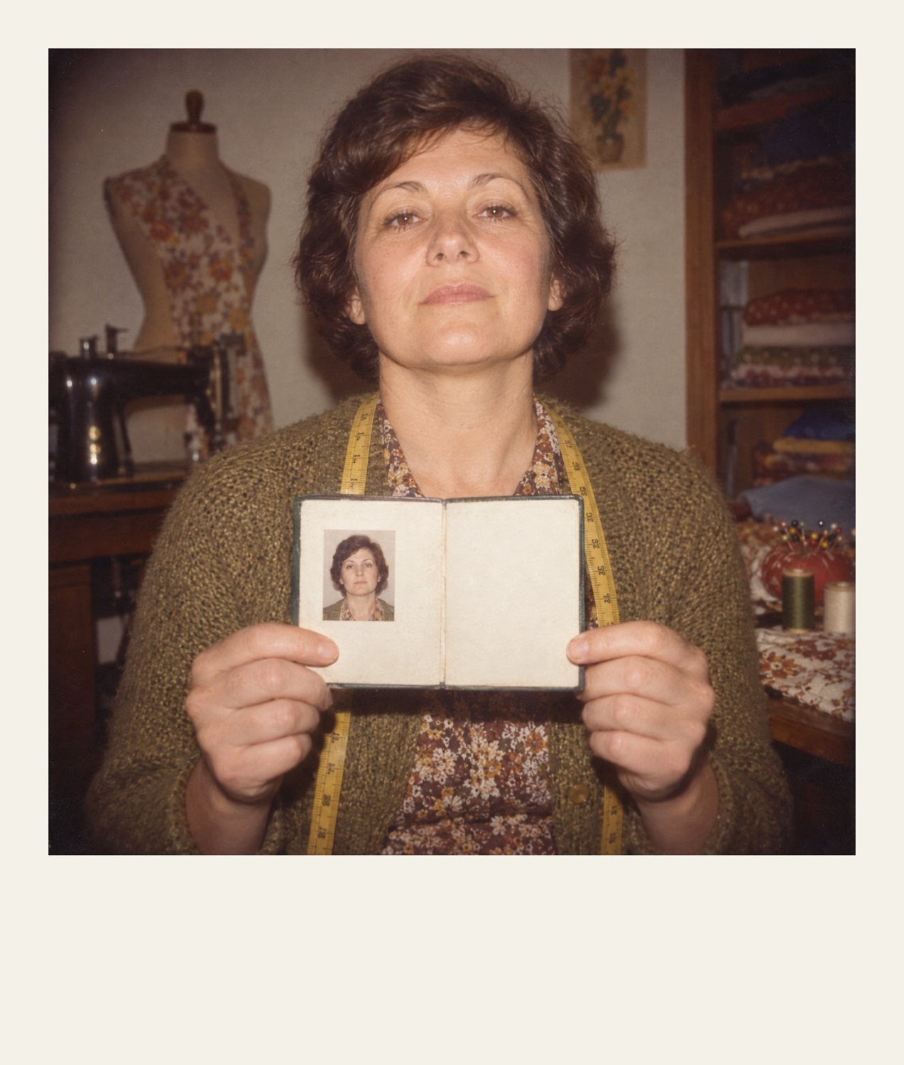 Polaroid of a seamstress holding up an identity booklet with her photo and no name