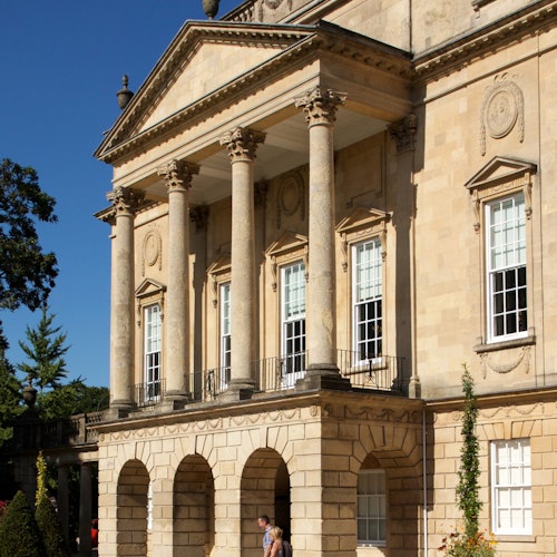 一座宏伟的建筑,拥有高大的柱子、拱形窗户和装饰性外墙。两个人正在入口附近走动。