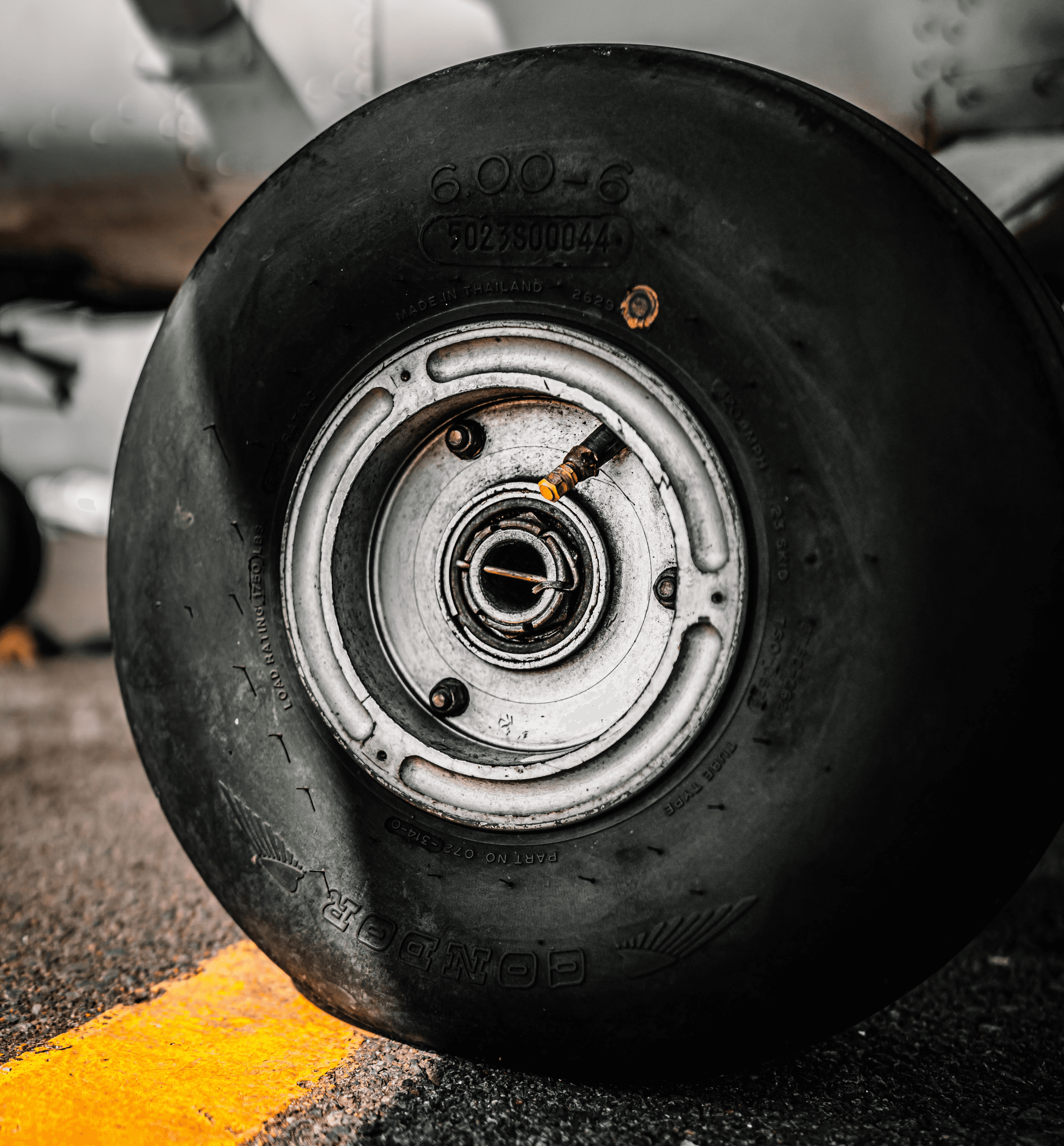 A close-up shot of a black aircraft tire with visible technical markings resting on an asphalt runway next to a yellow painted line