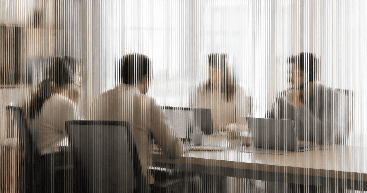 A small sales team making calls together in a bright office, seen through vertical fluted glass