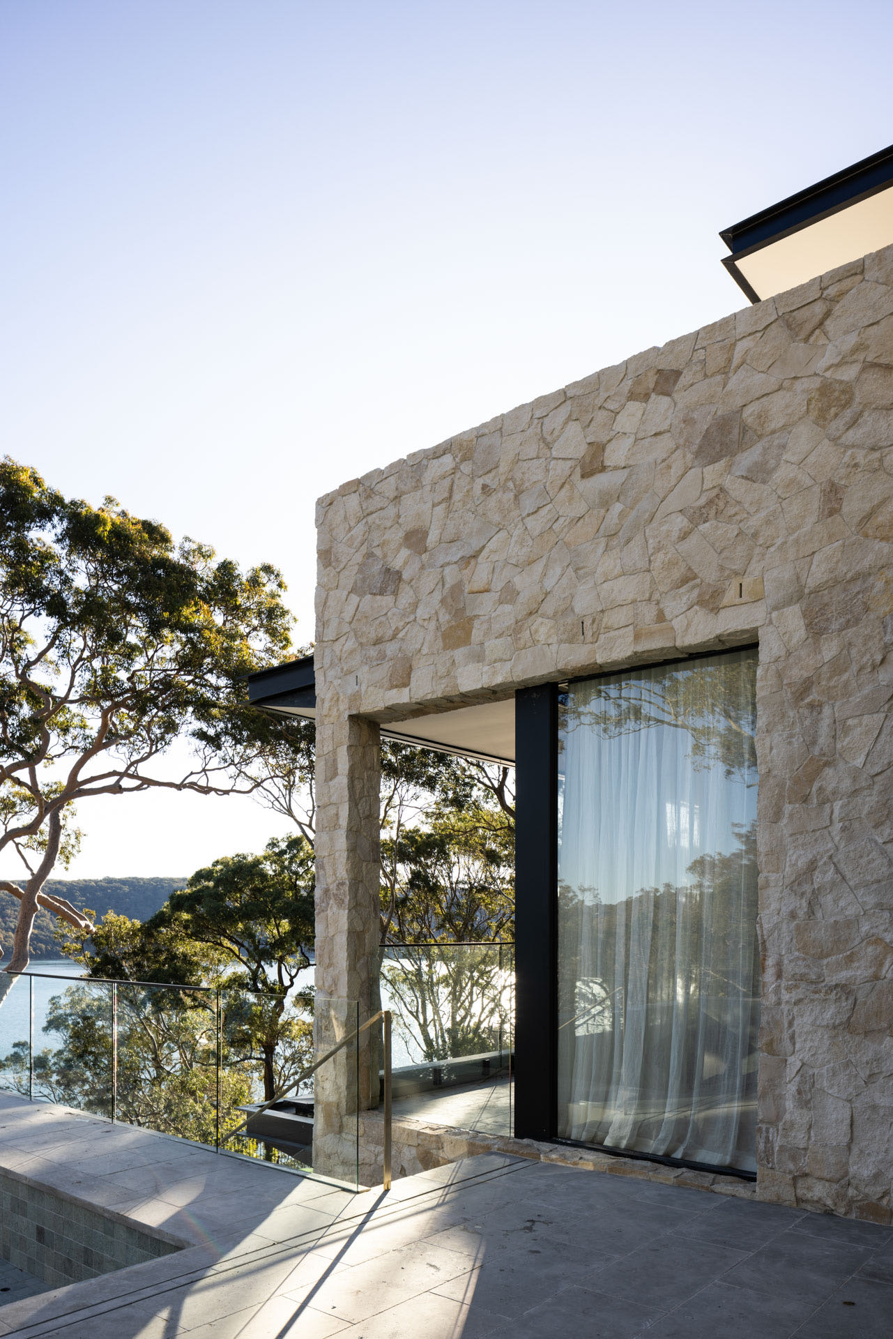 Modern glass and steel building with warm wooden ceilings, surrounded by lush greenery, blending contemporary architecture with nature.